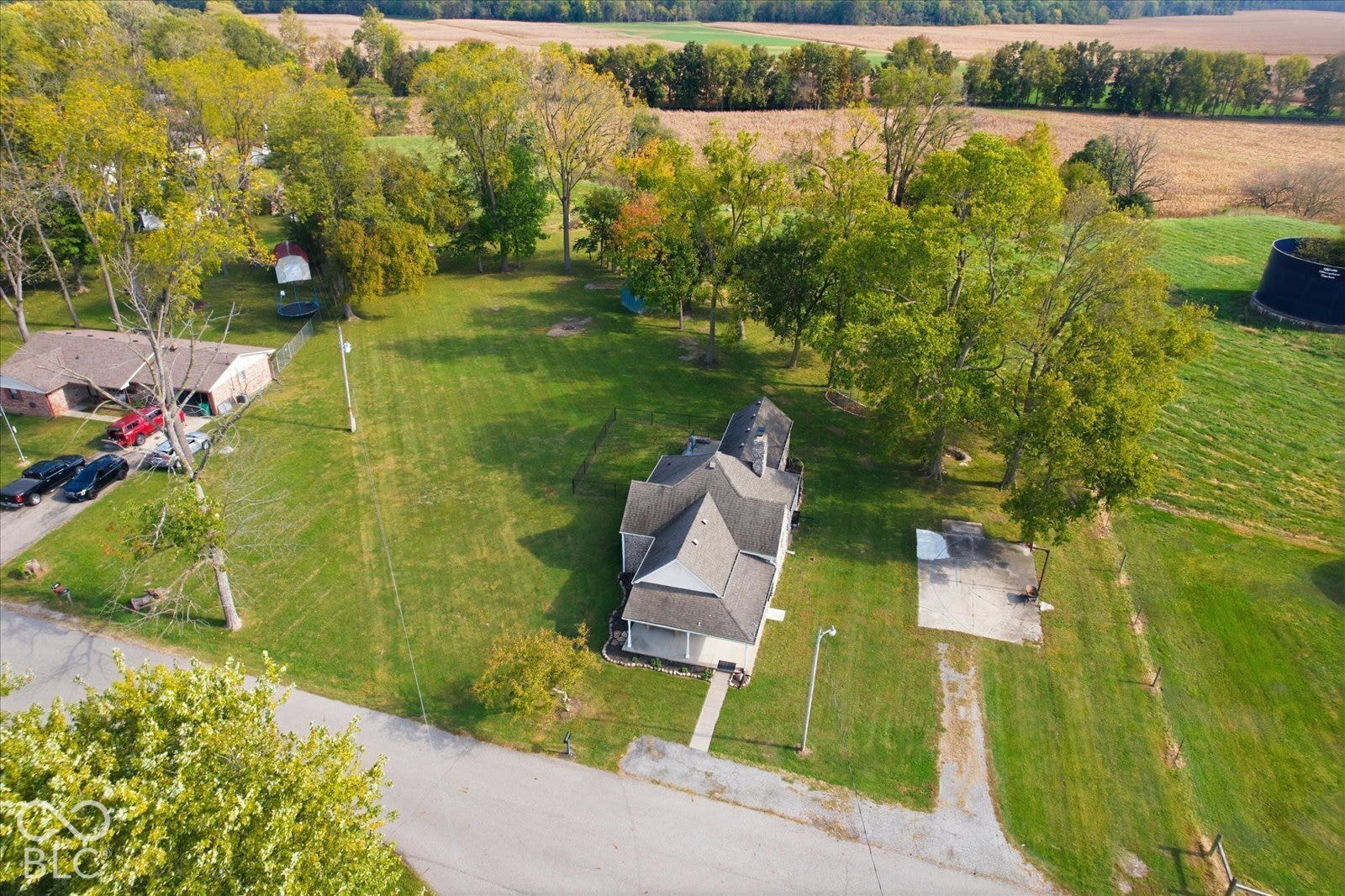 Aerial perspective of a multi-story residence situated on a lot featuring expansive green space, mature trees, a concrete pad, and asphalt driveway