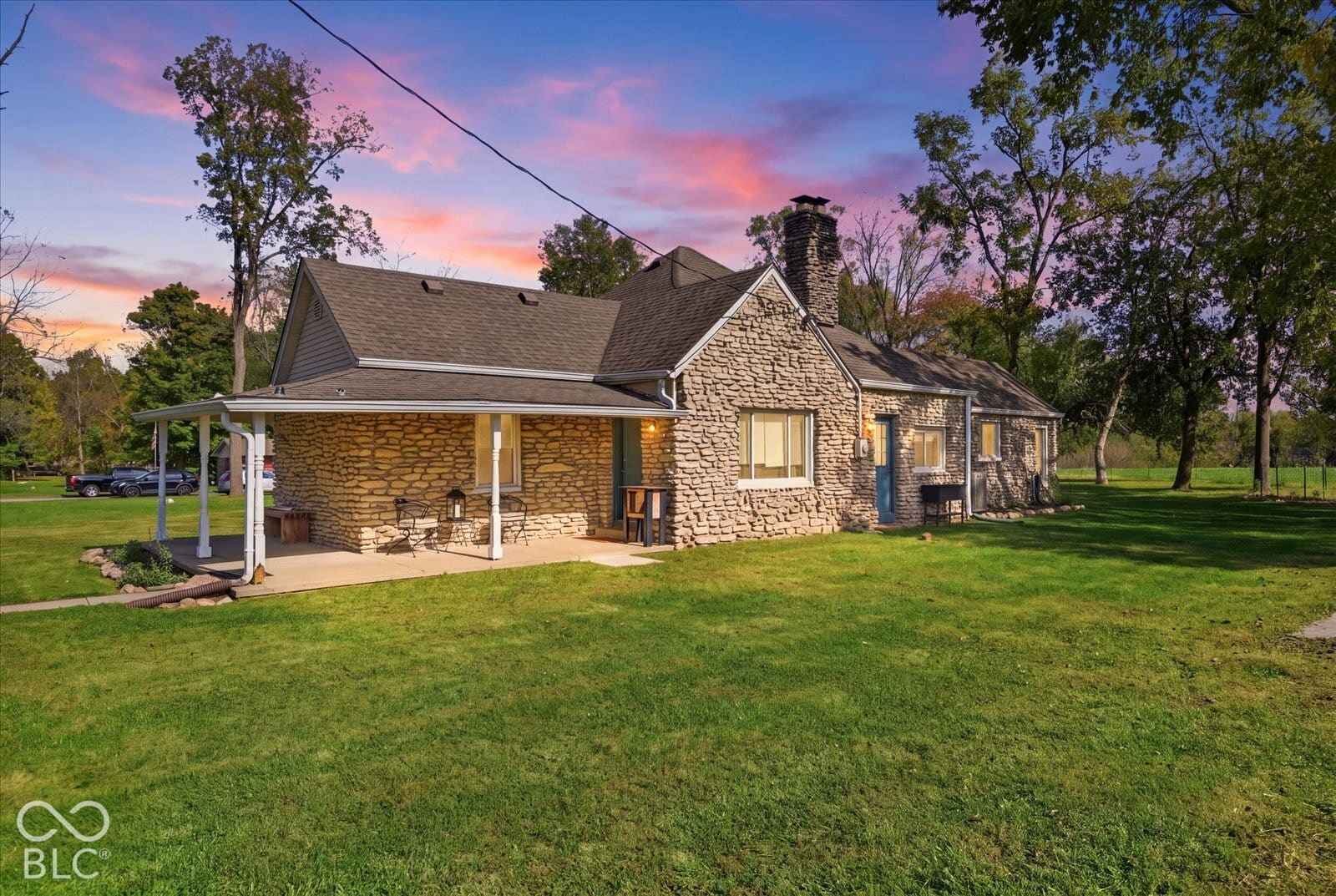 Virtually Altered - Exterior featuring natural stone masonry, covered front porch with white support posts, steep-pitched roofline, and an exterior stone chimney