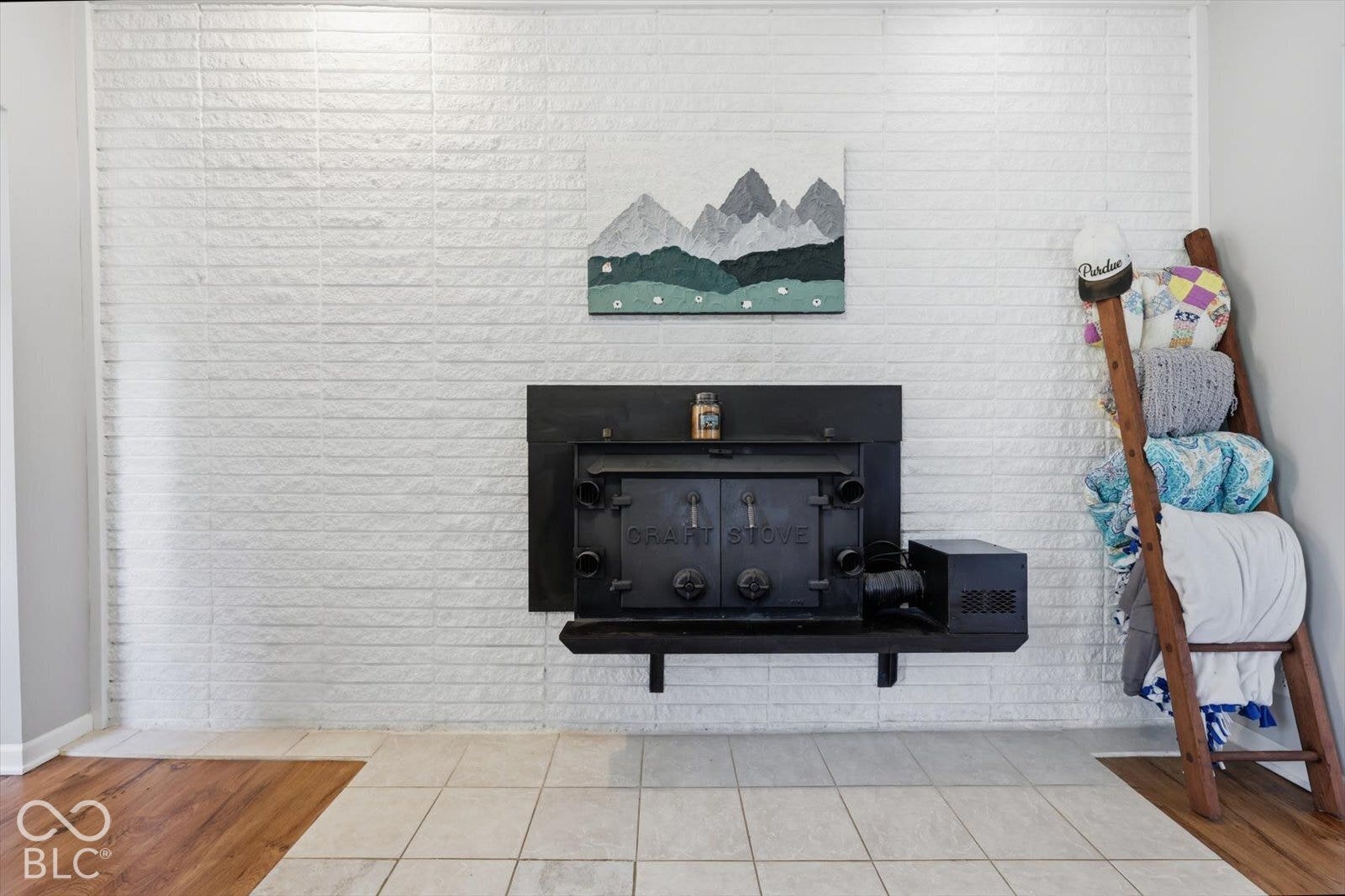 White-painted brick accent wall featuring a black cast-iron wood stove and square tile hearth