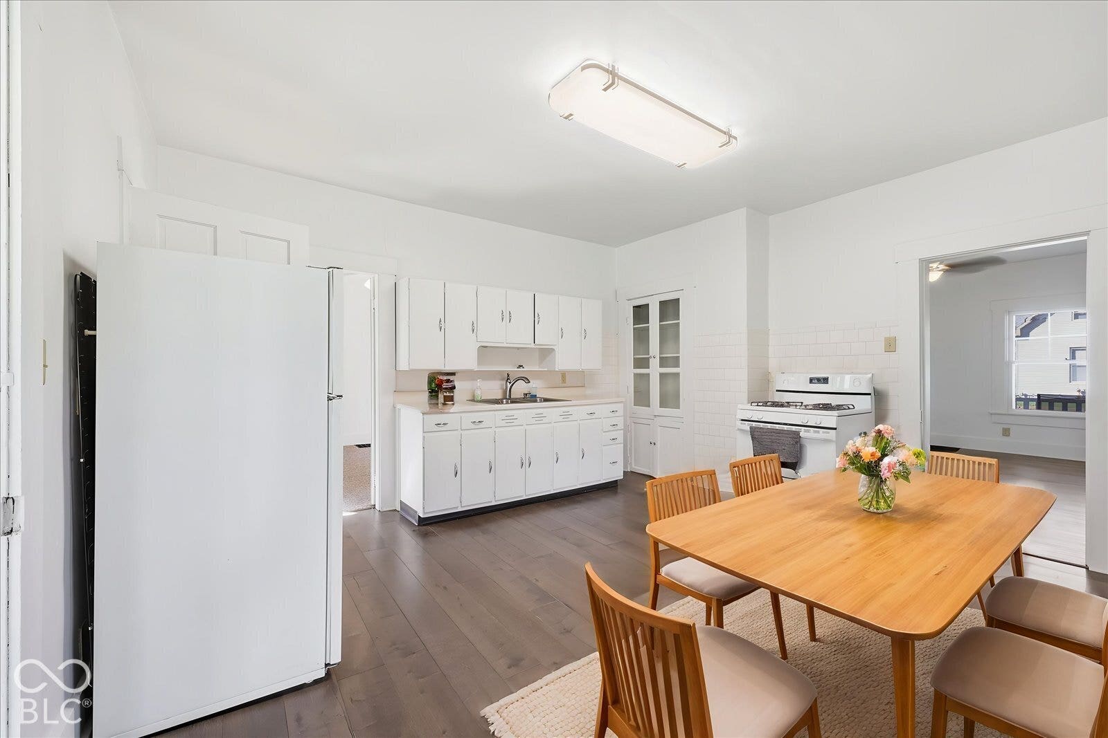 Virtually Altered - Kitchen featuring white cabinetry, built-in floor-to-ceiling pantry storage, wood-finish flooring, and subway tile backsplash