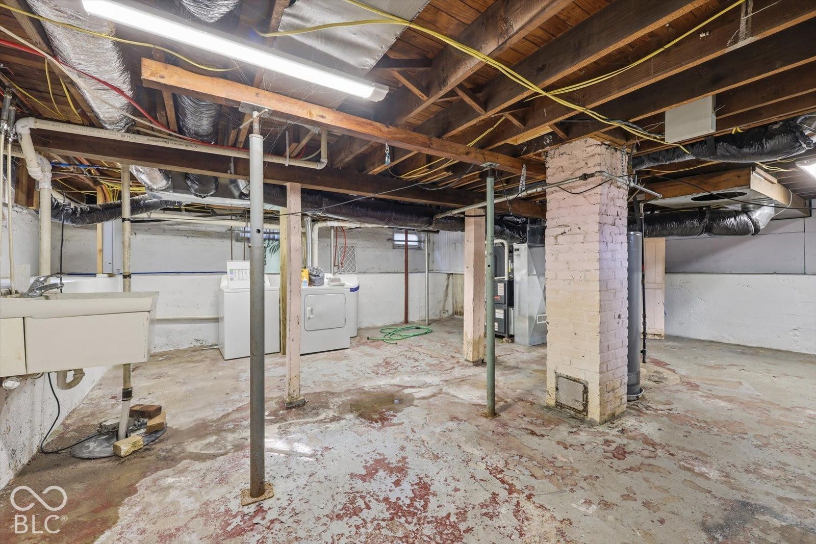 Unfinished basement featuring exposed joists, a central masonry support column, concrete flooring, and an integrated utility sink