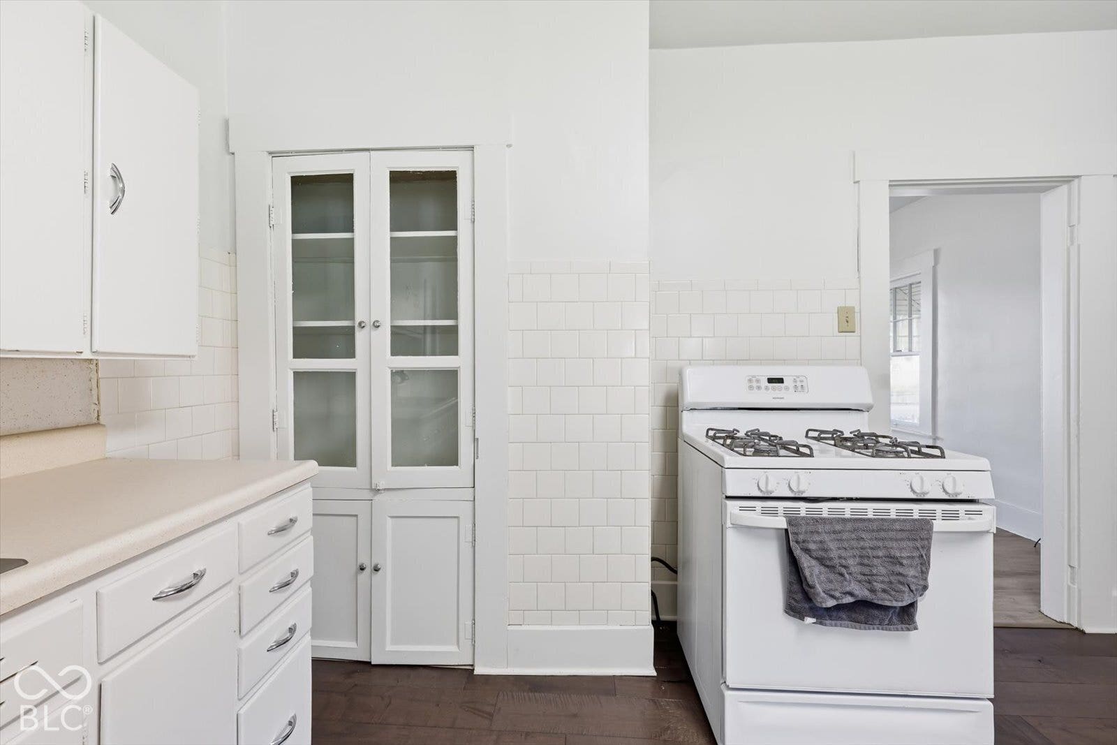 Kitchen featuring white cabinetry, built-in glass-front storage, white tile backsplash, and dark wood-finish flooring