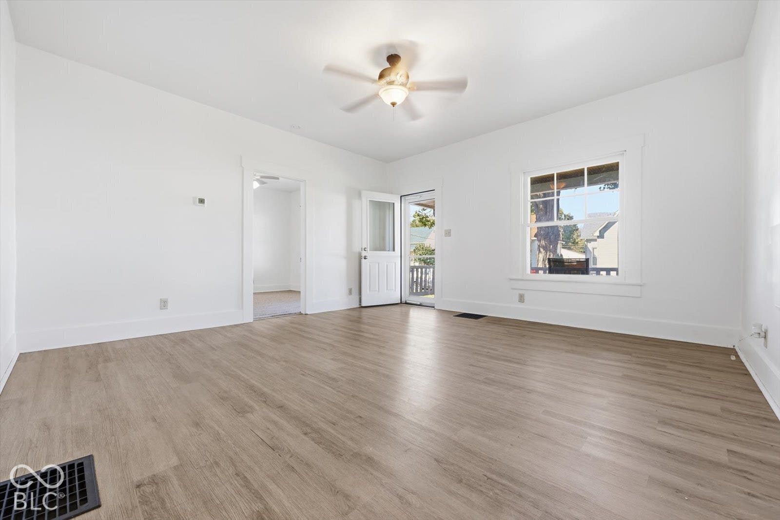 Interior room featuring light wood-finish flooring, white walls, a ceiling fan with integrated lighting, and a multi-pane window with wood trim