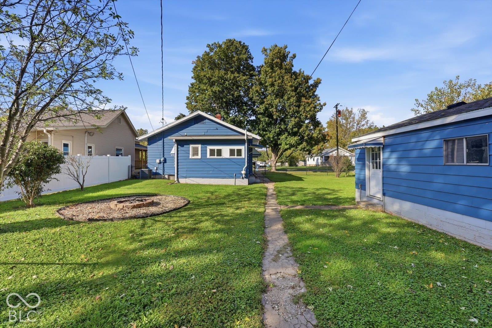 Backyard featuring a stone-lined fire pit, concrete walkway, detached structure with lap siding,