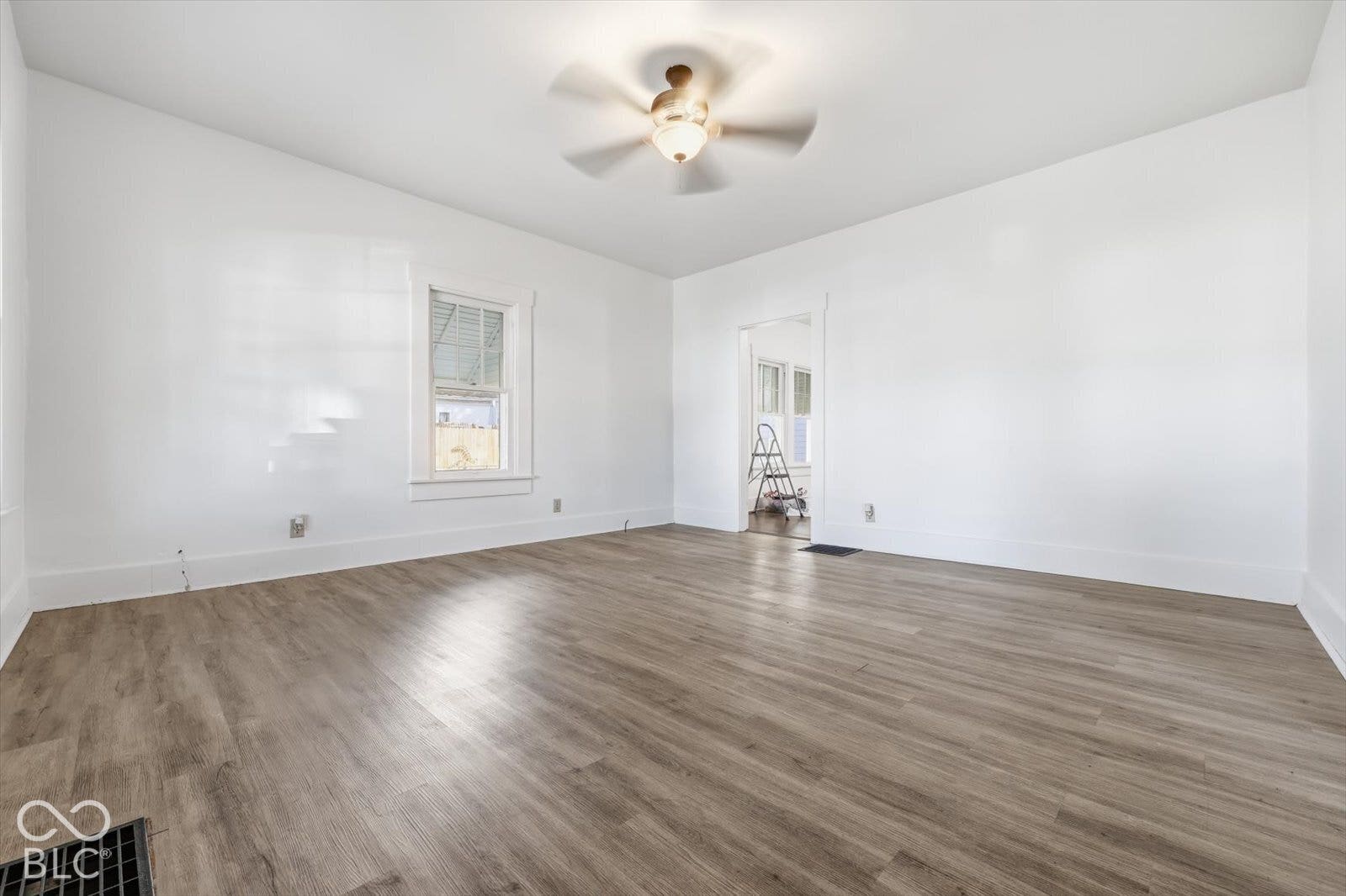 Neutral-toned wood-finish flooring, ceiling fan with light fixture, and double-hung window with white millwork casing