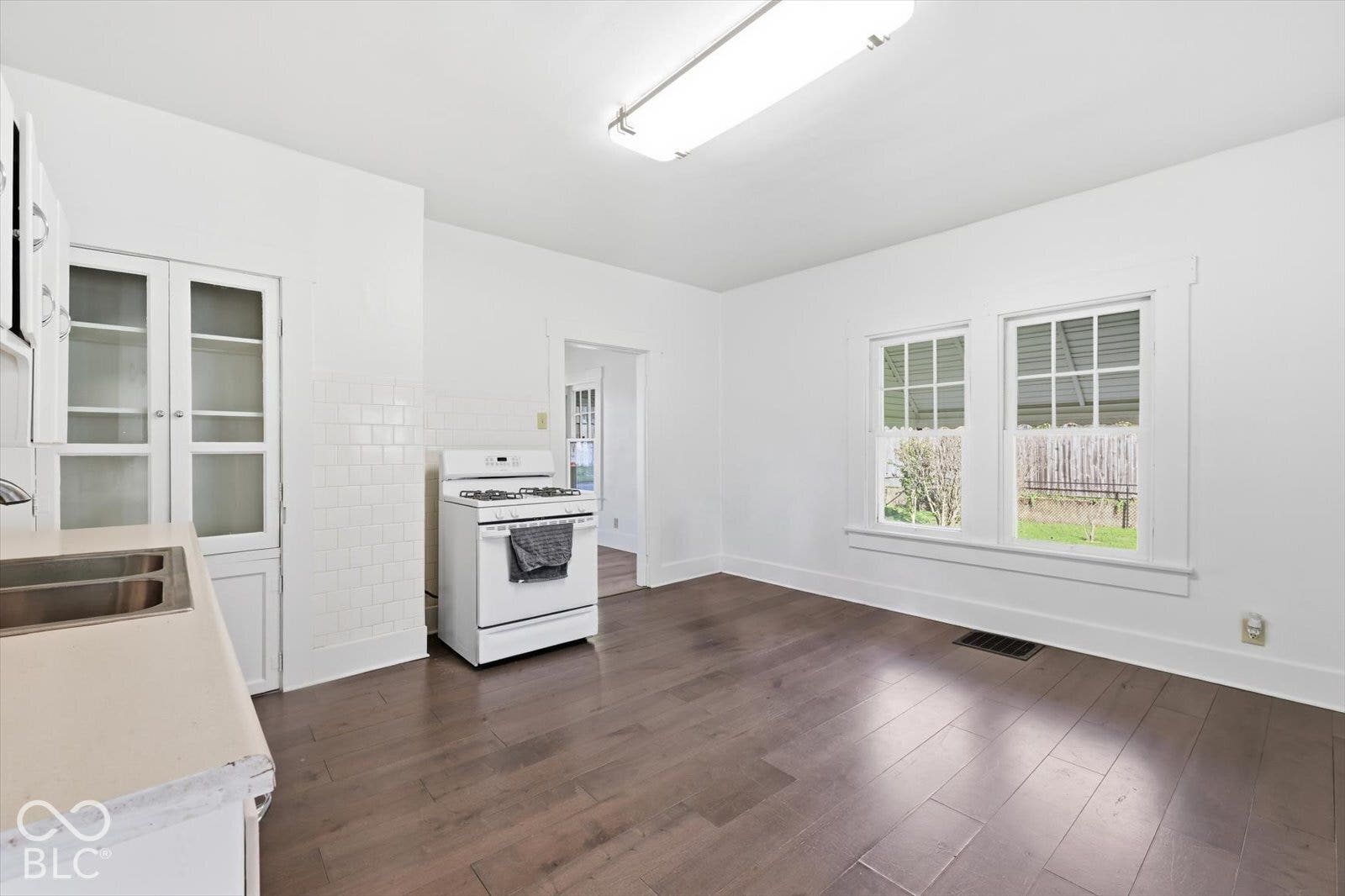 Kitchen area featuring wood-finish flooring, built-in glass-front cabinetry, subway tile backsplash, and dual double-hung windows