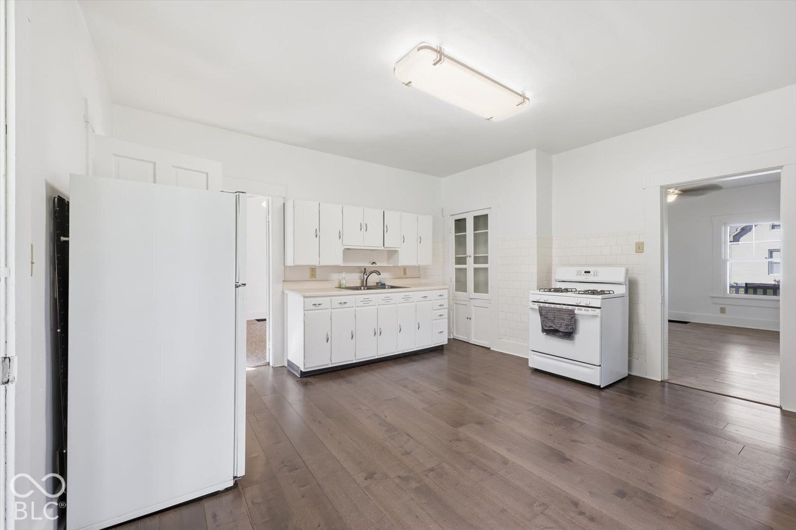 Kitchen featuring wood-finish flooring, white cabinetry, integrated glass-front pantry, white tile backsplash