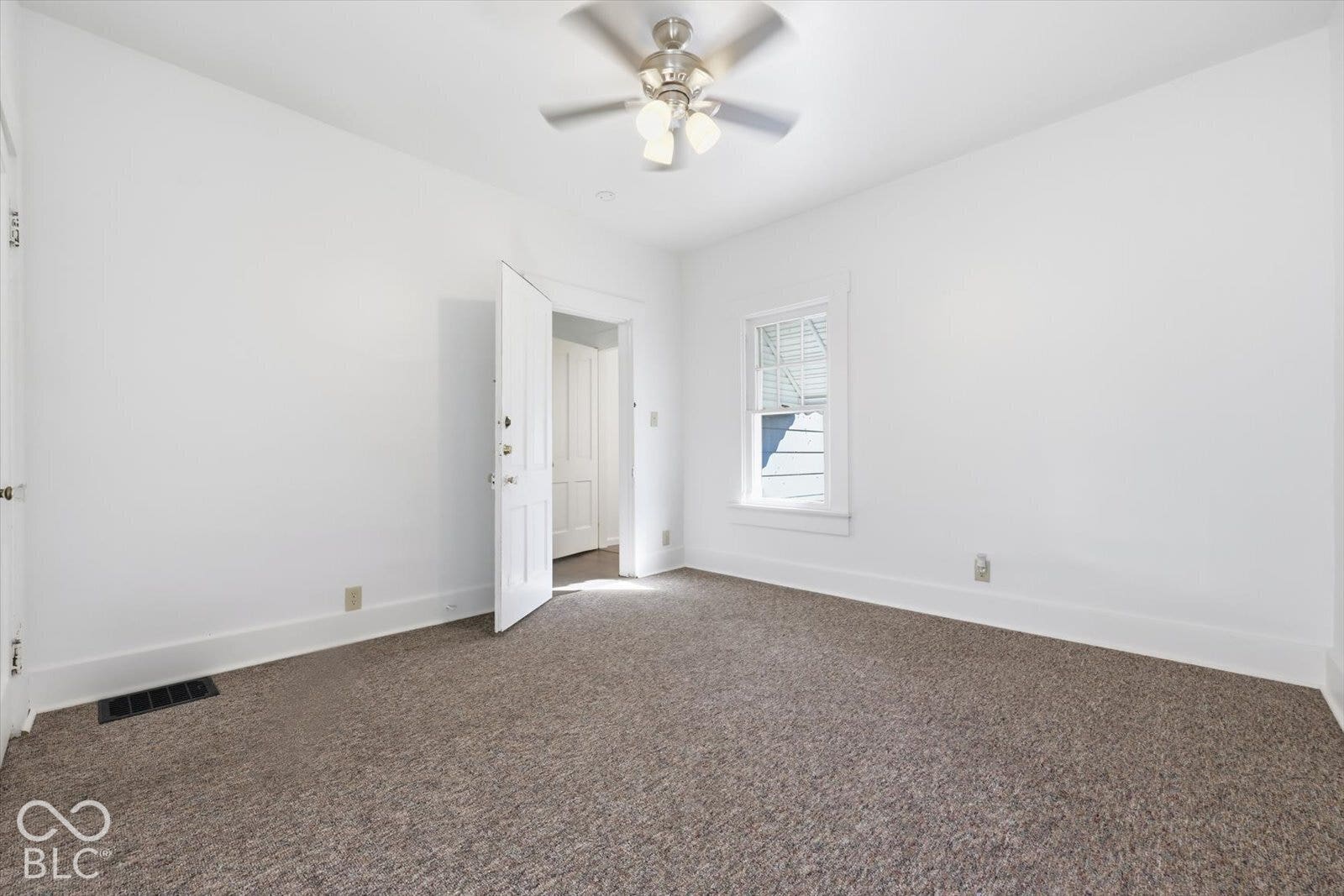 Interior space featuring neutral-toned carpeting, a multi-light ceiling fan, and a double-hung window with casing