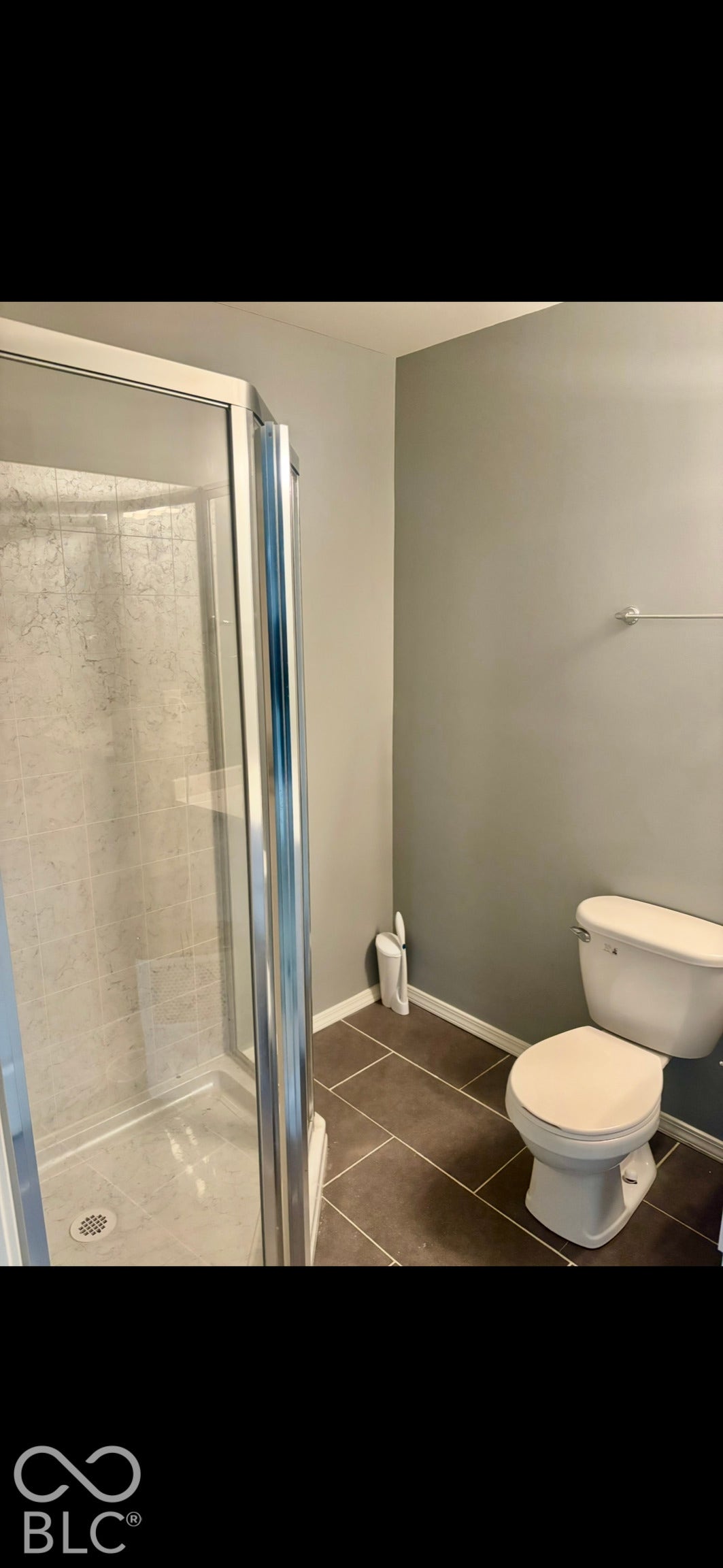 Corner glass shower enclosure with neutral wall surround and dark-toned ceramic tile flooring