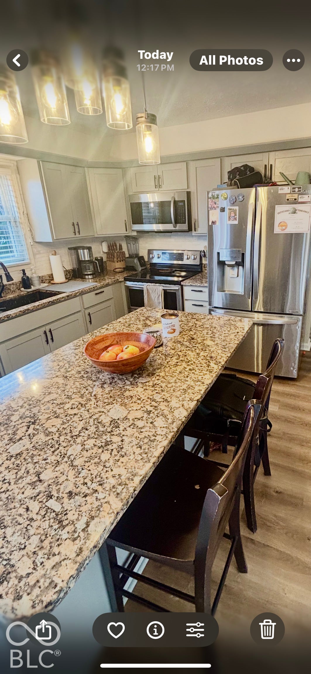 Kitchen featuring a central island with stone countertop, stainless steel refrigerator and microwave, wood-finish flooring, and pendant lighting