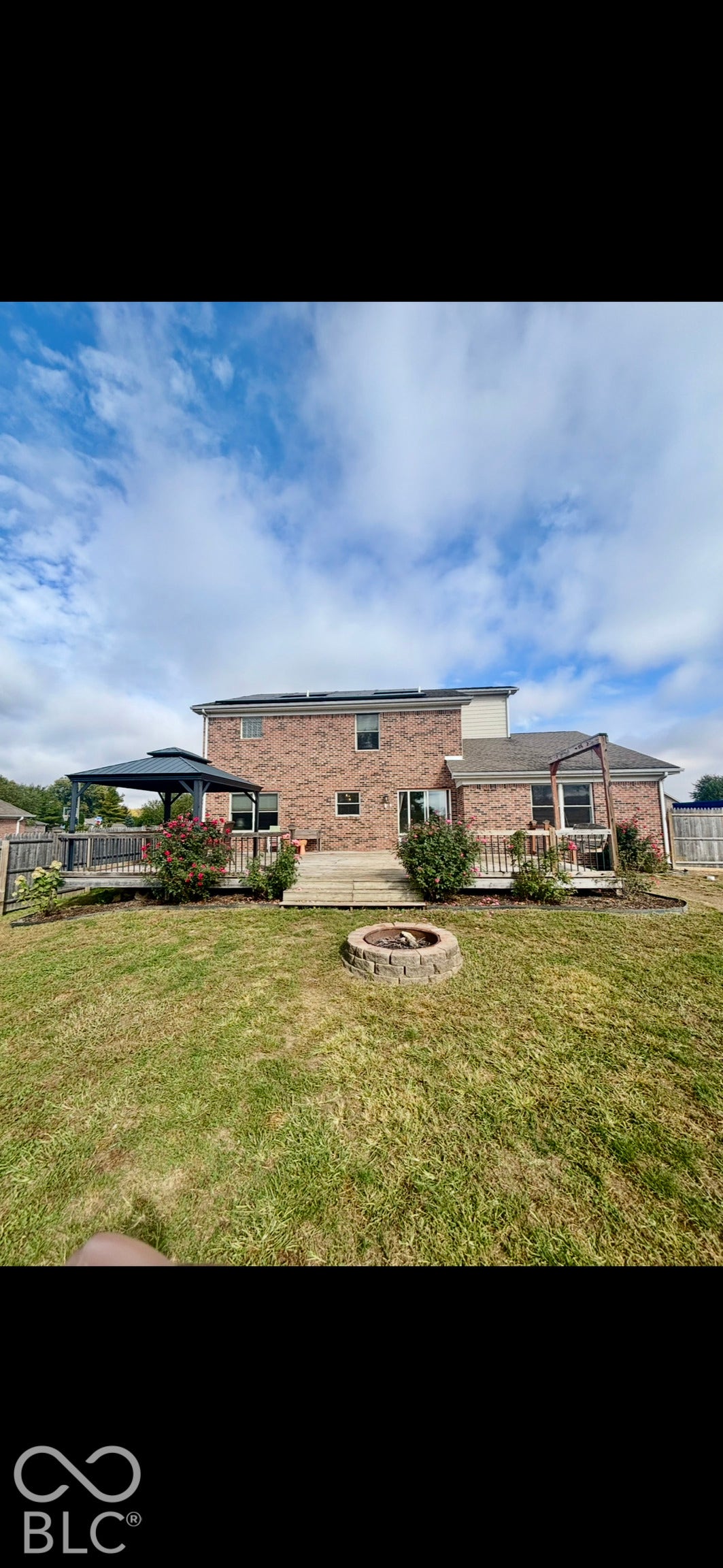 Brick exterior, expansive wooden deck with railing, integrated fire pit, and level lawn
