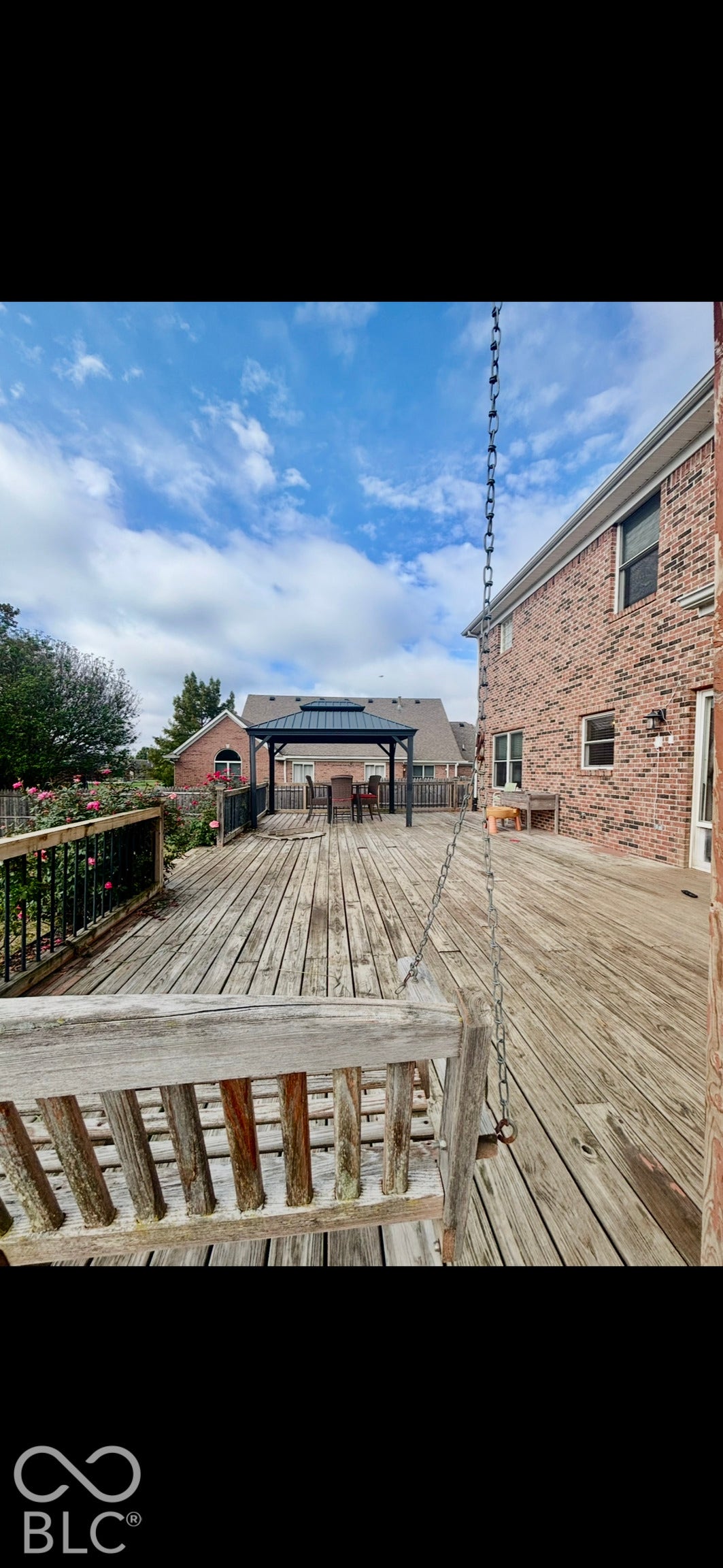 Expansive wood deck featuring a hanging wood bench, black metal railing, and a detached metal-frame gazebo