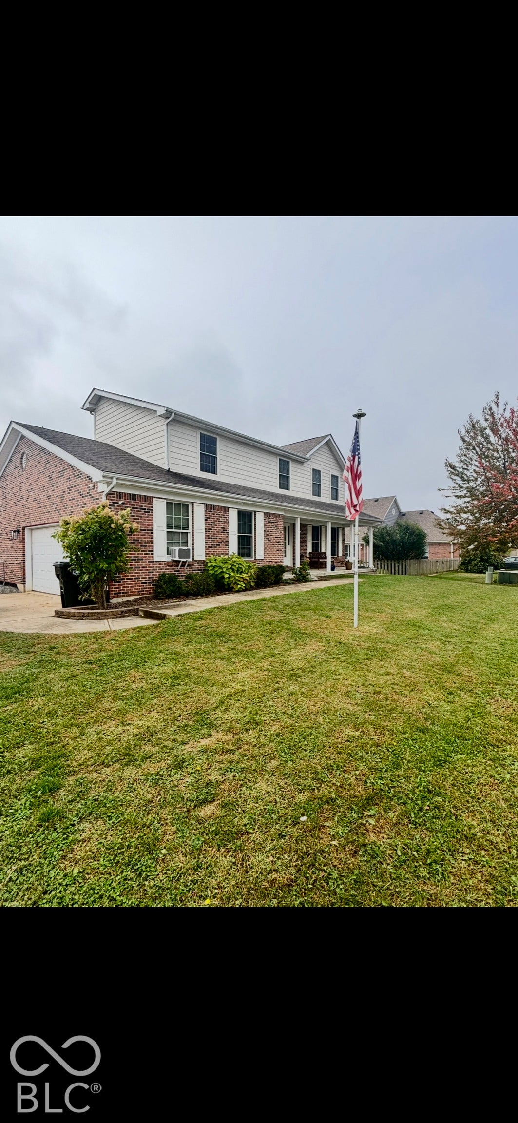 Two-story colonial exterior featuring brick and horizontal siding, a covered front porch, an attached garage, and a lawn