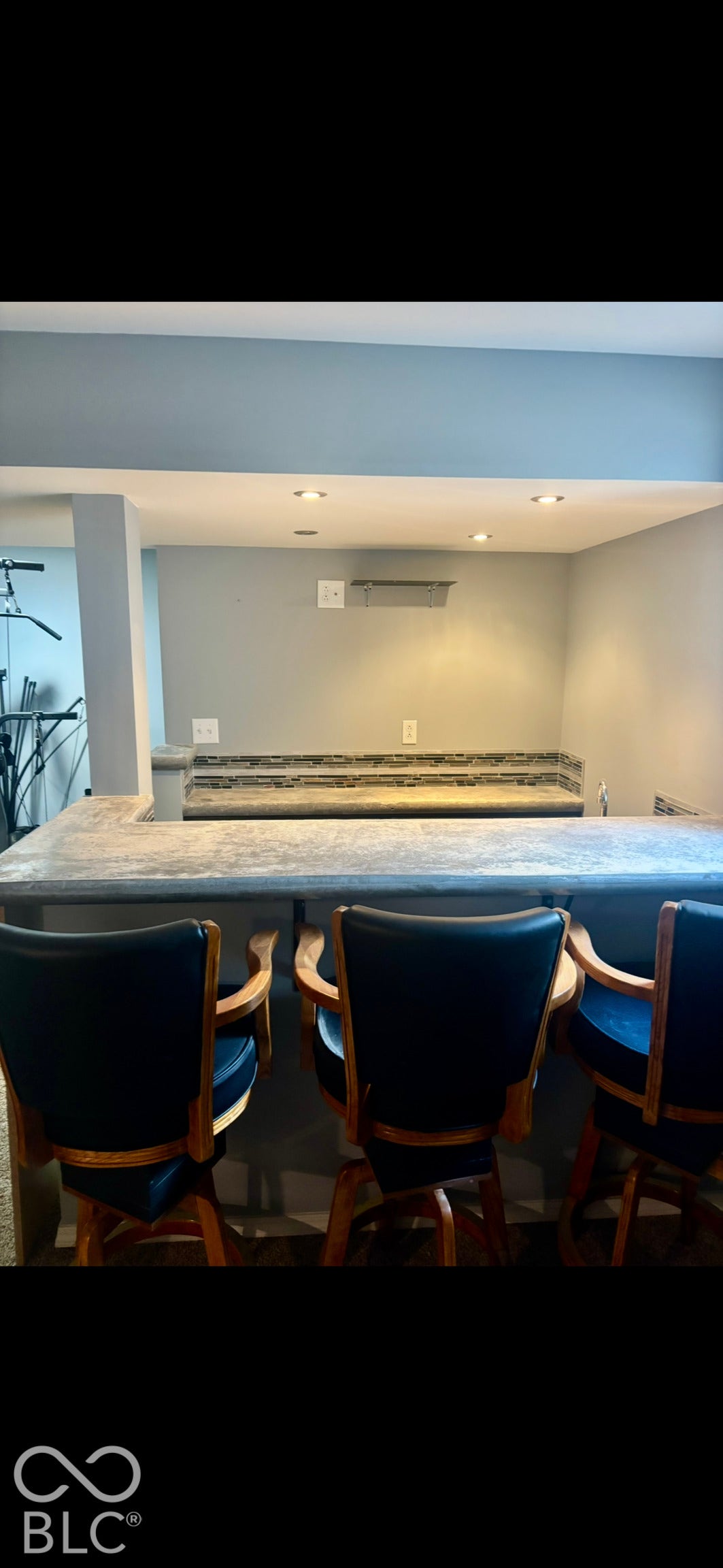 Built-in wet bar featuring a textured concrete-finish countertop, stone tile backsplash, recessed ceiling lighting, and neutral wall color