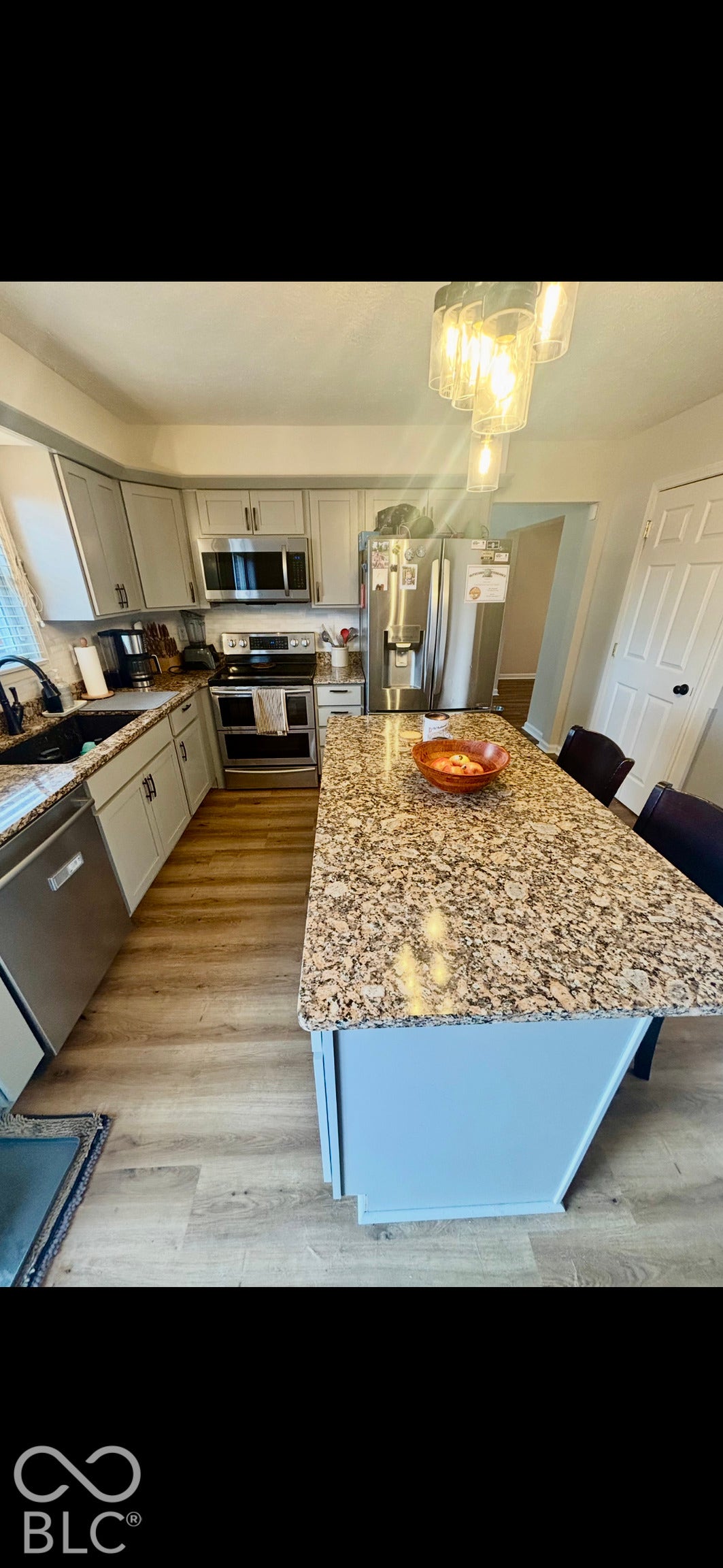Kitchen featuring a center island with a stone countertop, light-toned shaker cabinetry, stainless steel appliances, and wood-finish flooring