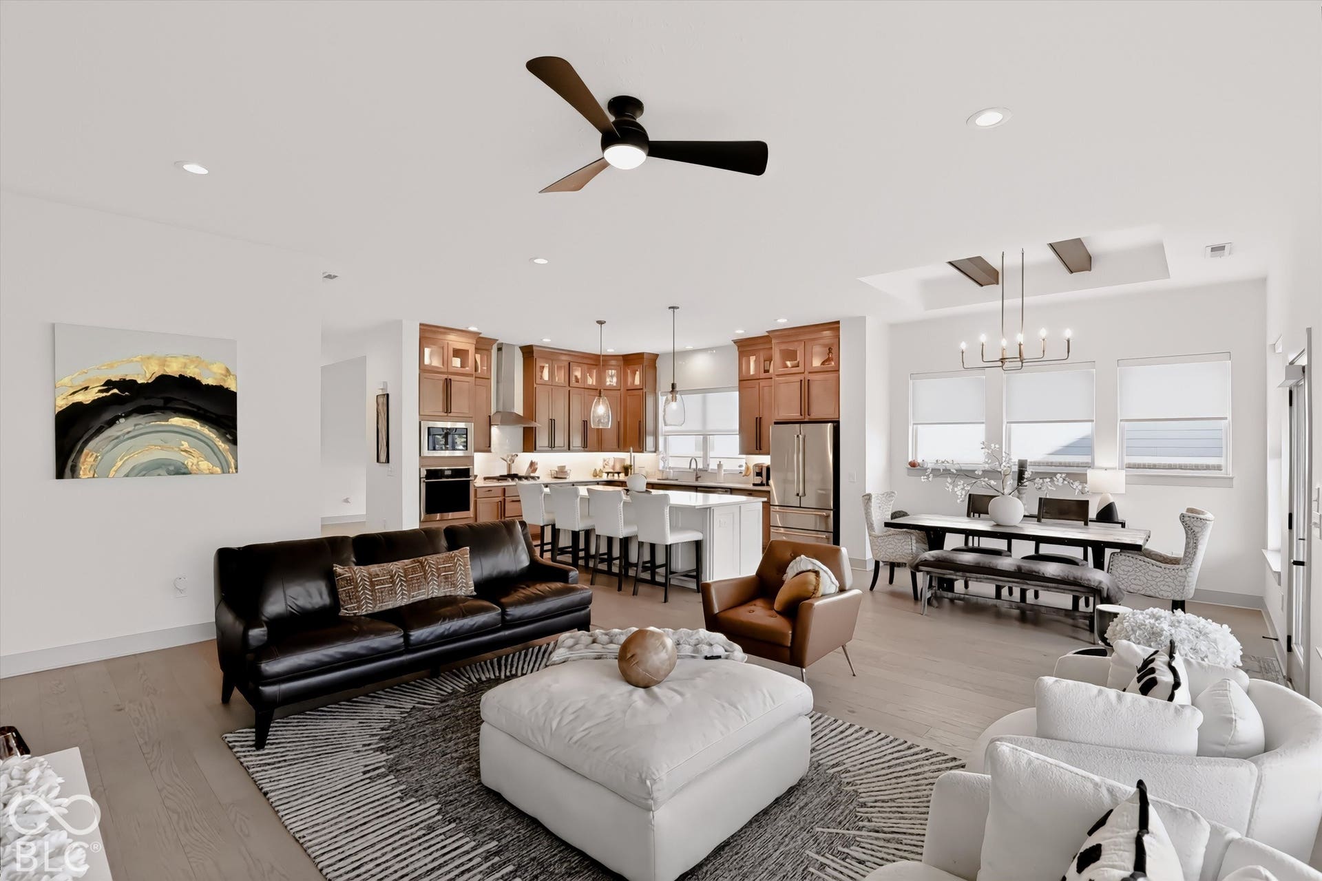 Open-concept interior featuring wood-finish flooring, a kitchen with cabinetry and an island, a recessed ceiling with wooden beam details, and a modern ceiling fan