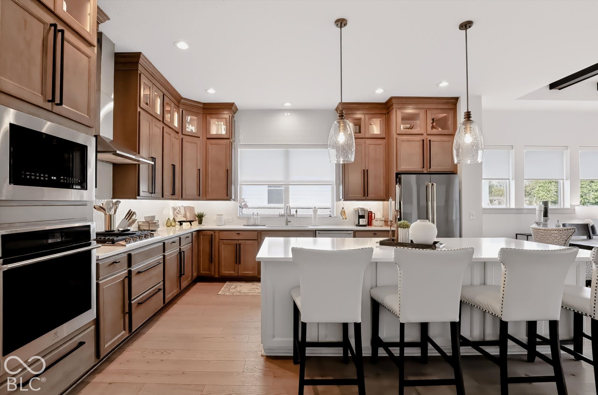 Kitchen featuring stained wood cabinetry, quartz countertops, a central island with bar seating, stainless steel appliances, and glass pendant lighting