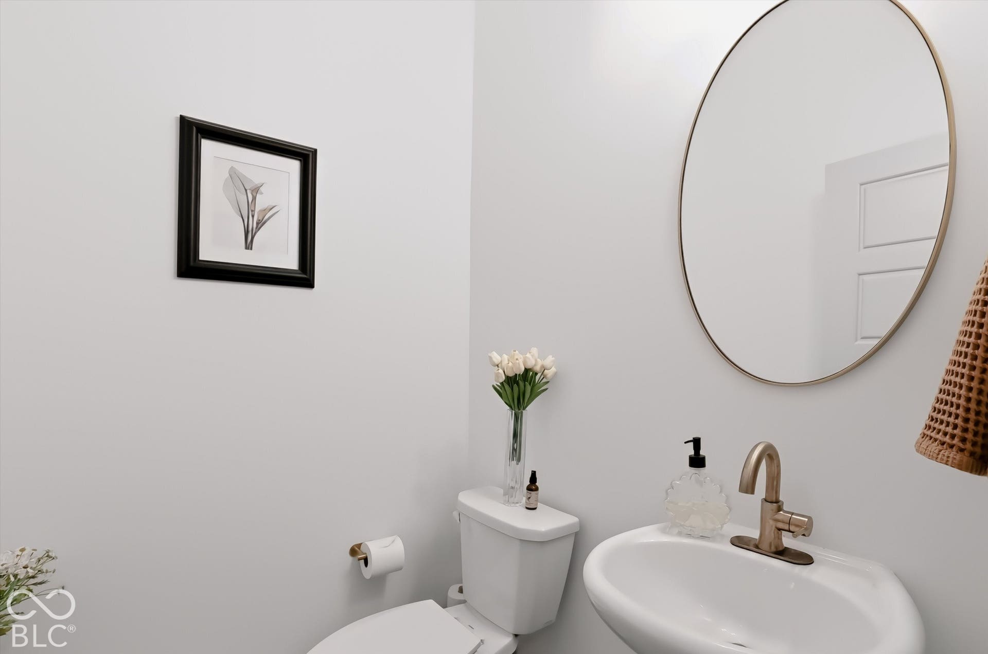 Oval wall-mounted mirror with a metallic frame, pedestal sink with a gold-tone finish faucet, and coordinating gold-tone hardware