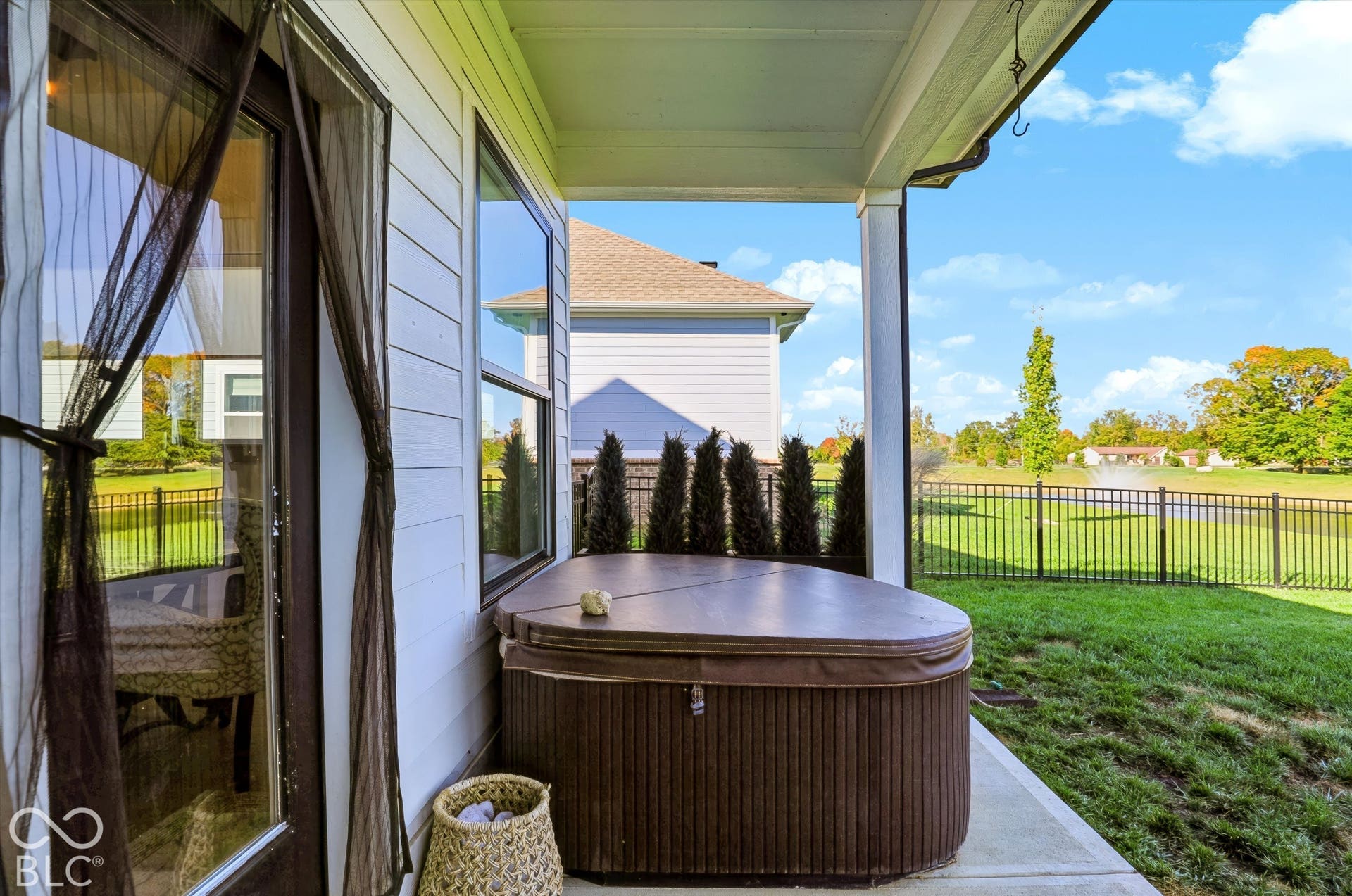 Covered concrete patio featuring a built-in spa, horizontal lap siding, and metal perimeter fencing