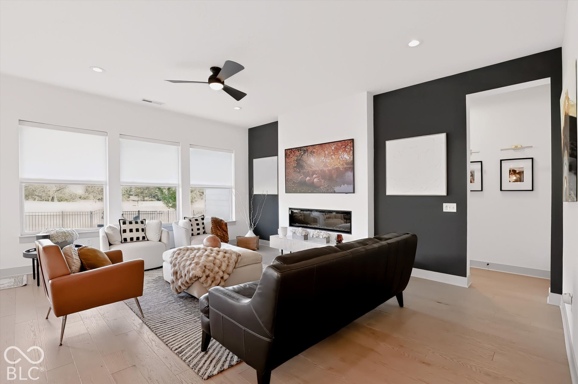 Living area featuring wood-finish flooring, a linear built-in fireplace, three expansive windows, and a matte black ceiling fan