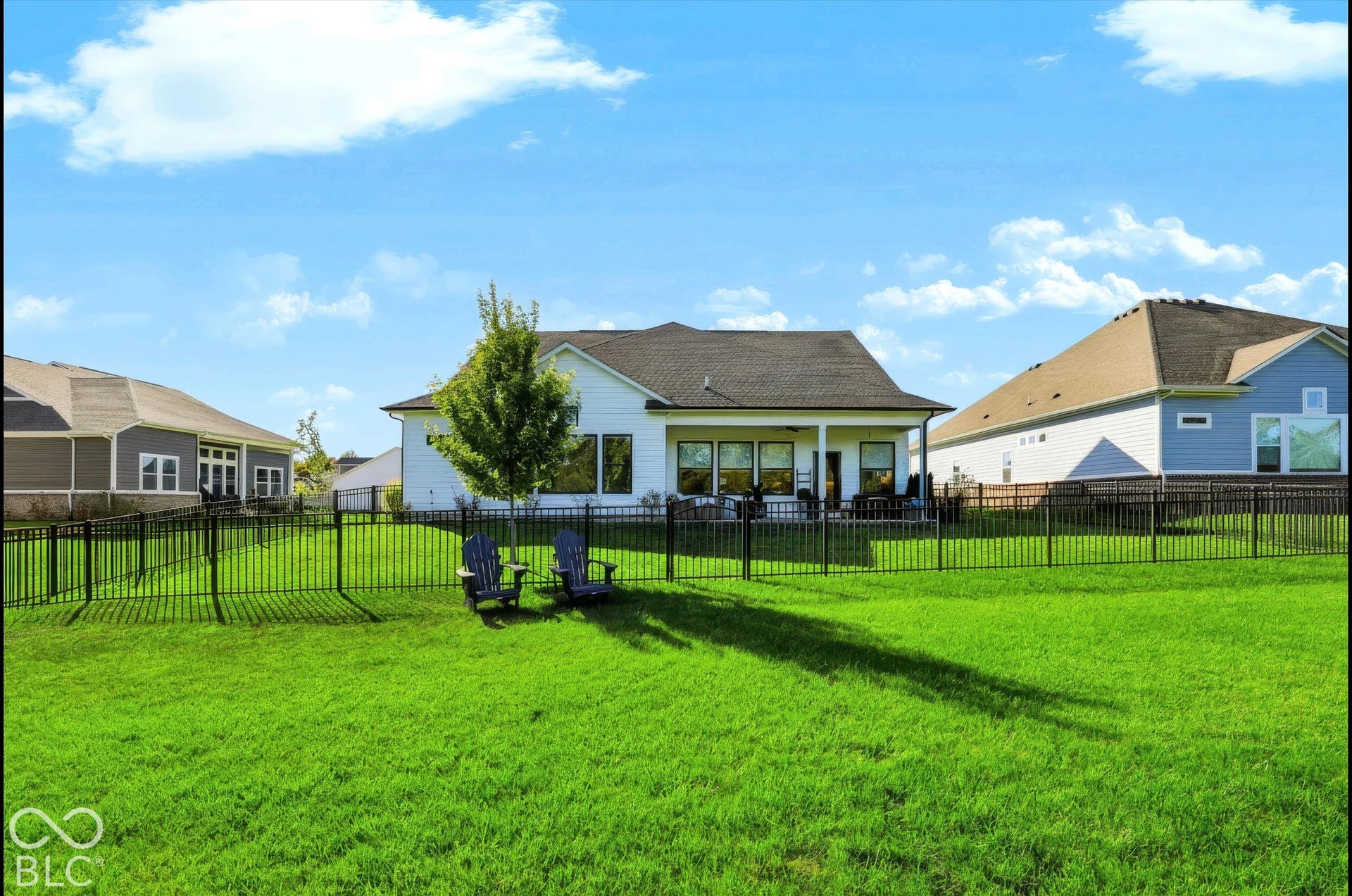 Rear exterior featuring a covered patio, metal perimeter fencing, and a manicured lawn