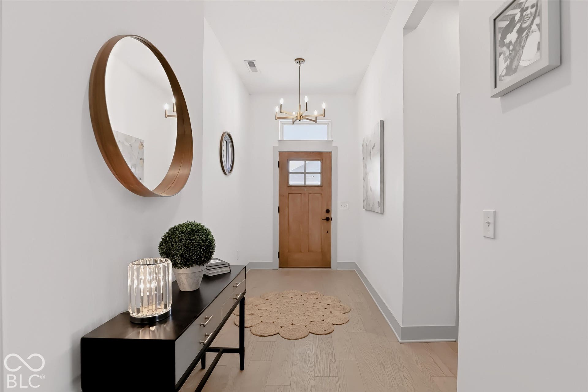 Entryway featuring wood-finish flooring, a solid wood front door with a transom window, and a multi-arm candle-style chandelier