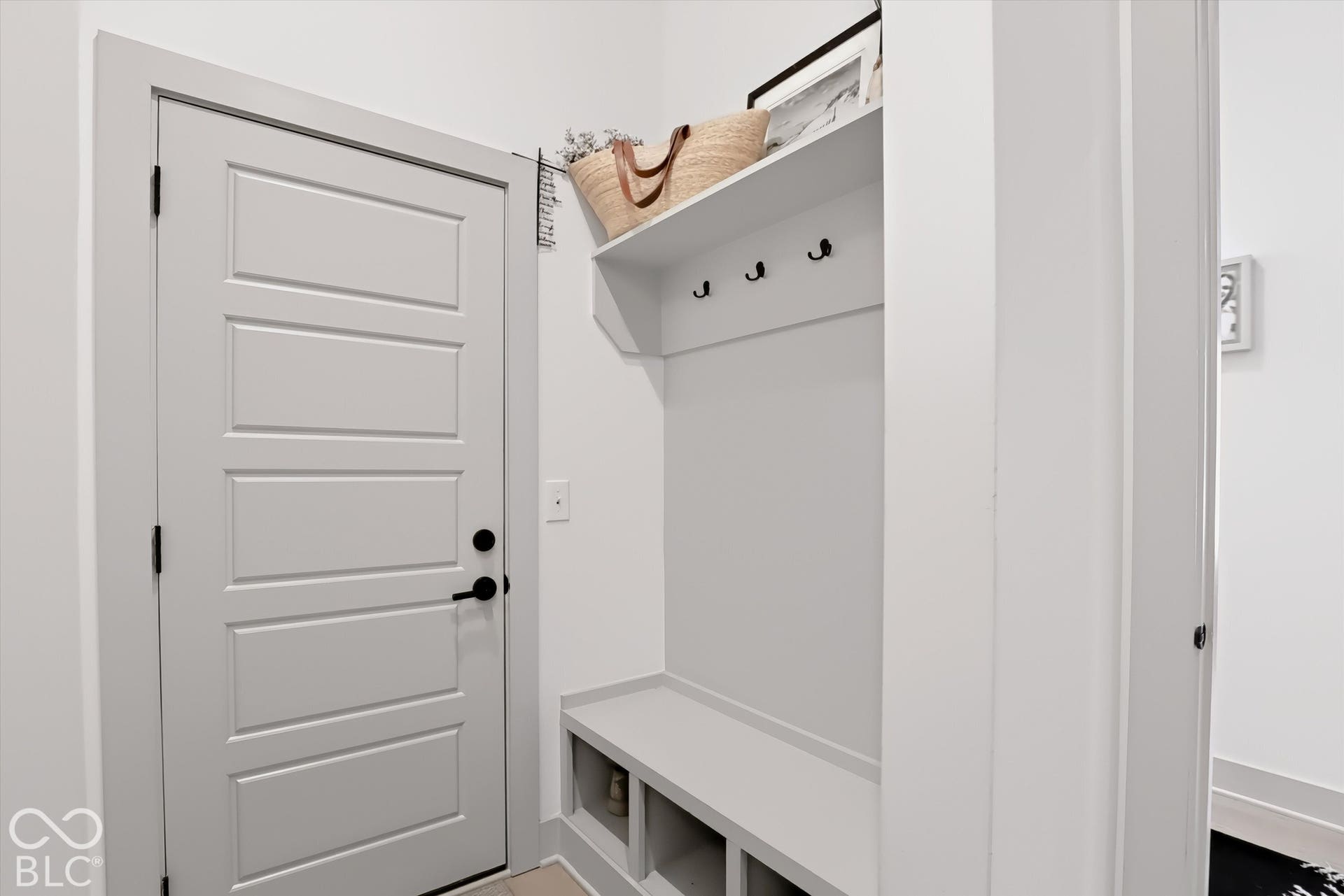 Built-in bench with integrated cubbies, overhead shelving, matte black hardware, and a four-panel interior door