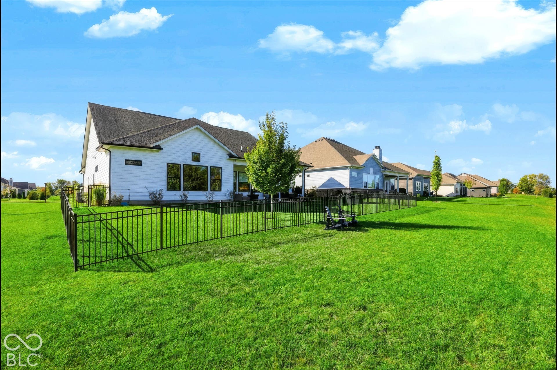 White horizontal siding exterior with a dark-shingle roof, featuring an expansive rear lawn enclosed by black metal fencing