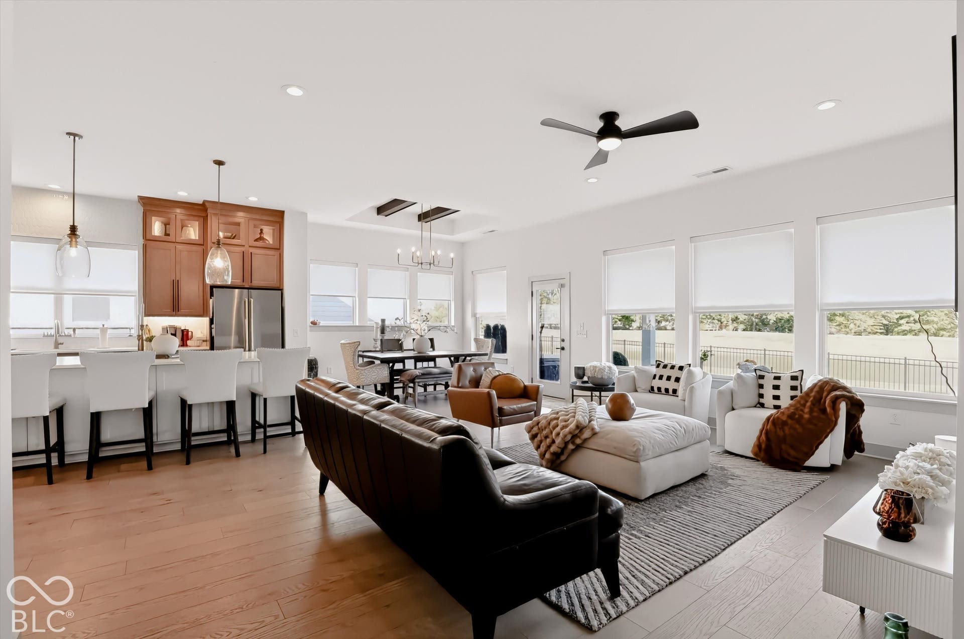 Open-concept interior featuring wood-finish flooring, recessed lighting, a coffered ceiling with exposed wood beams, and large windows with roller shades