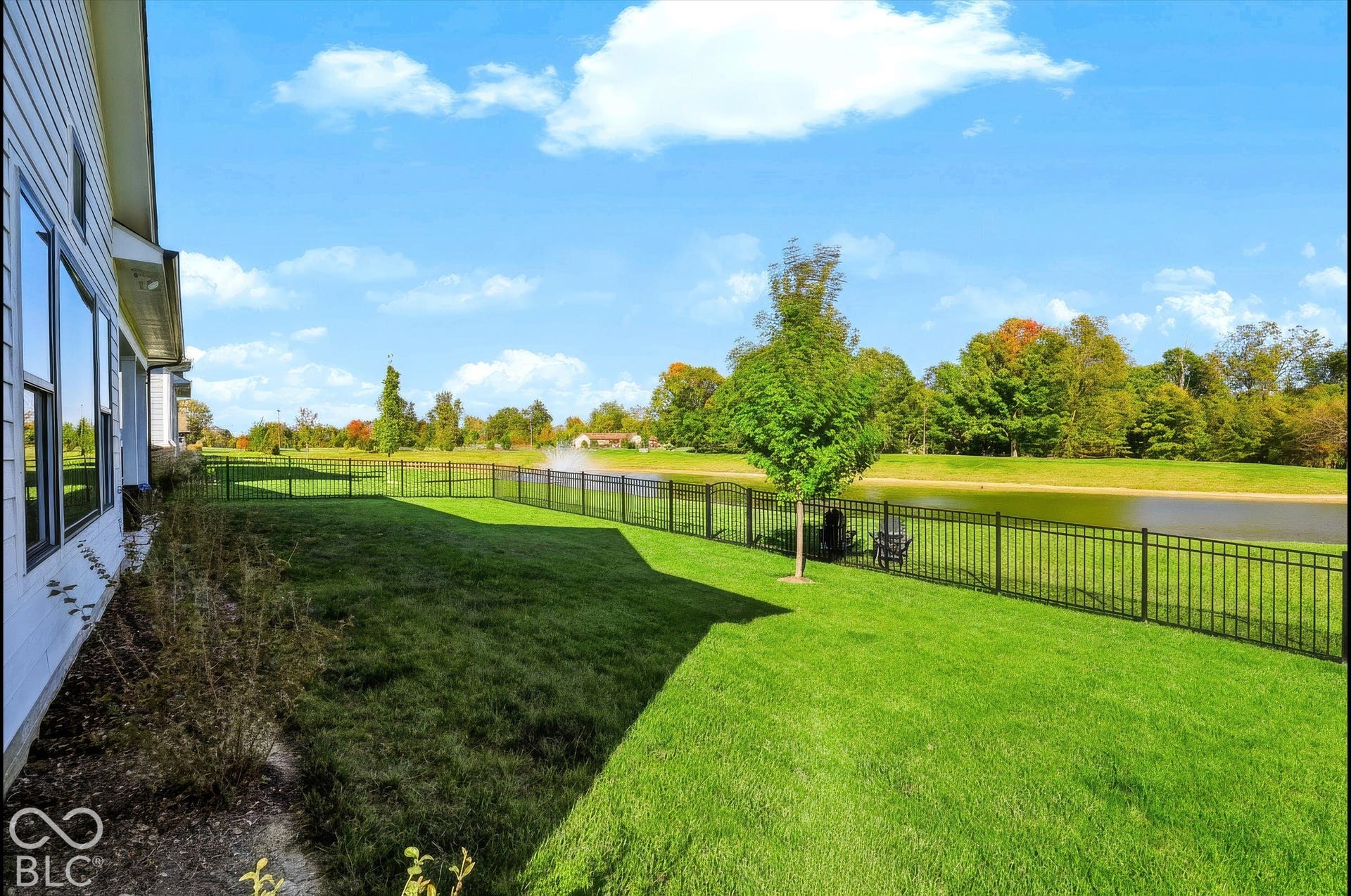 Expansive backyard featuring a manicured lawn, perimeter metal fencing, and water frontage with a decorative fountain