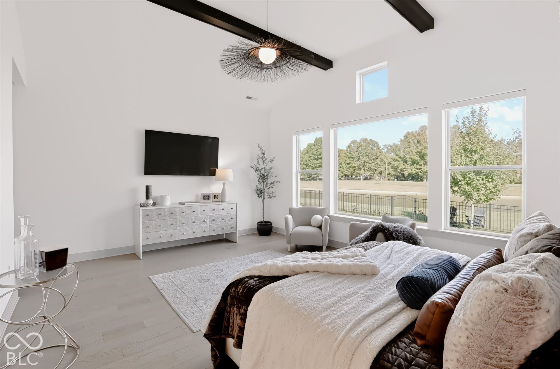 Vaulted ceilings featuring exposed dark-finish decorative beams, expansive windows, and light-toned wood-finish flooring