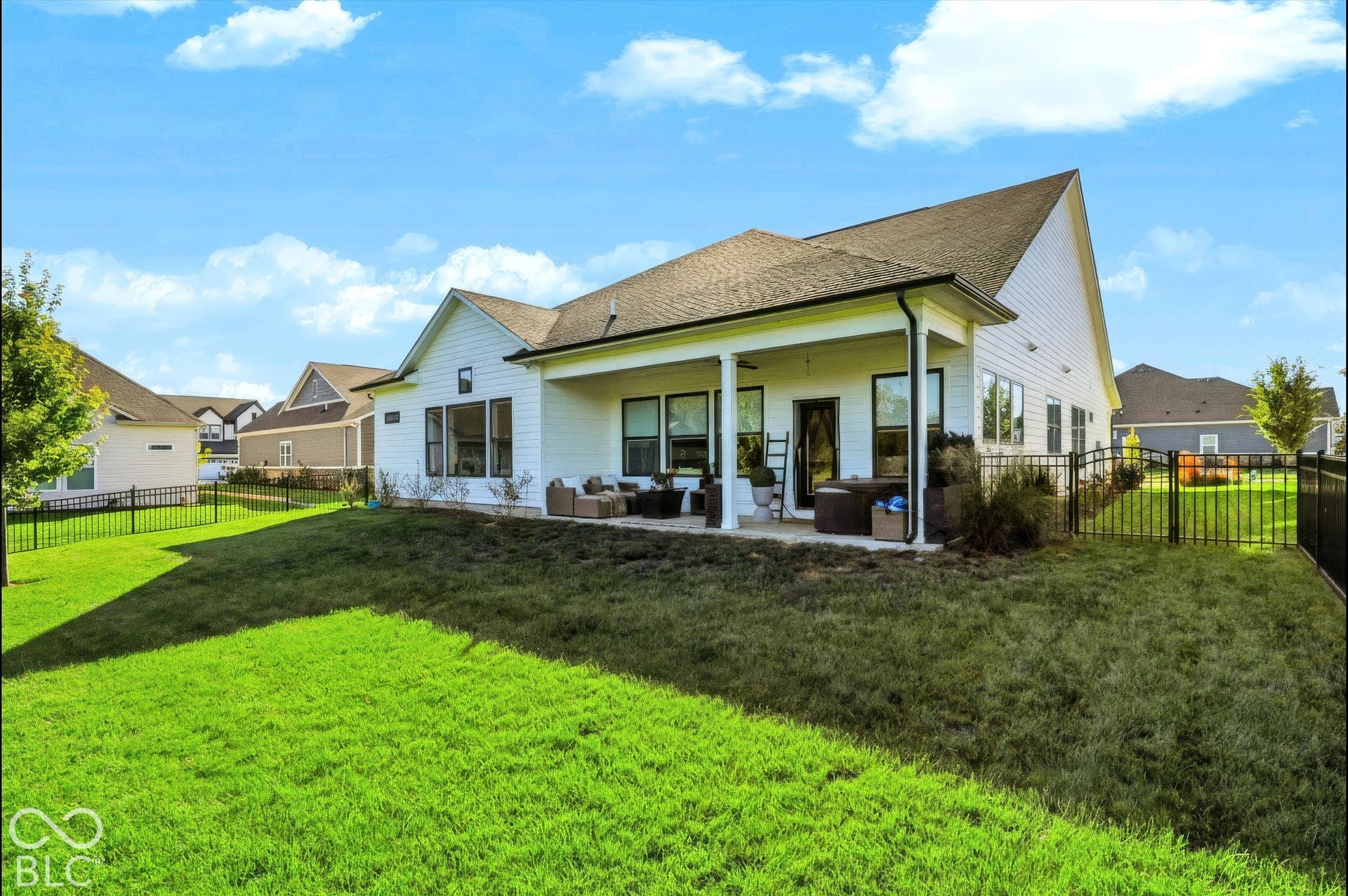 Rear exterior featuring white horizontal siding, a covered concrete patio, and a fully fenced backyard with a manicured lawn