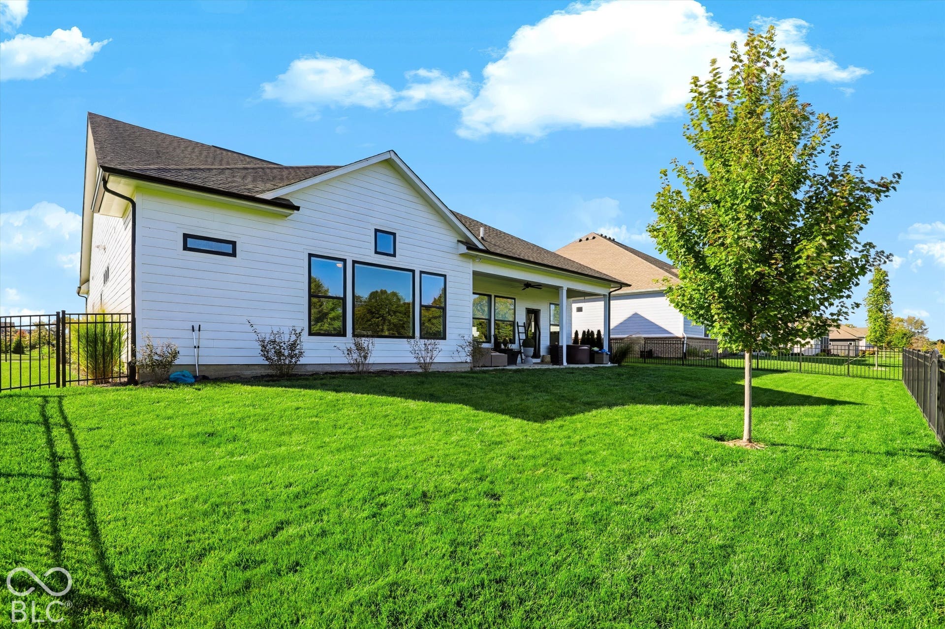 White horizontal siding exterior with a covered patio, large windows, and a metal perimeter fence enclosing the grass yard