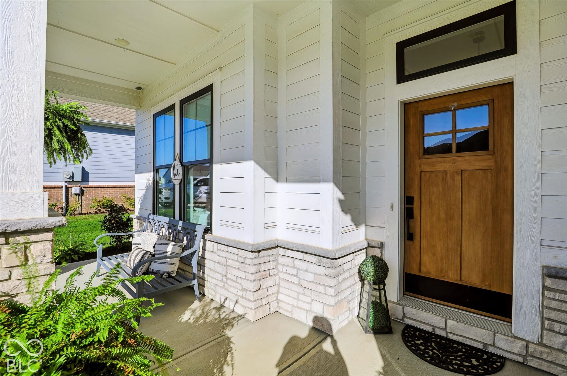 Covered front porch featuring horizontal lap siding, stone veneer base detailing, and a natural wood-finish front door with an inset transom window