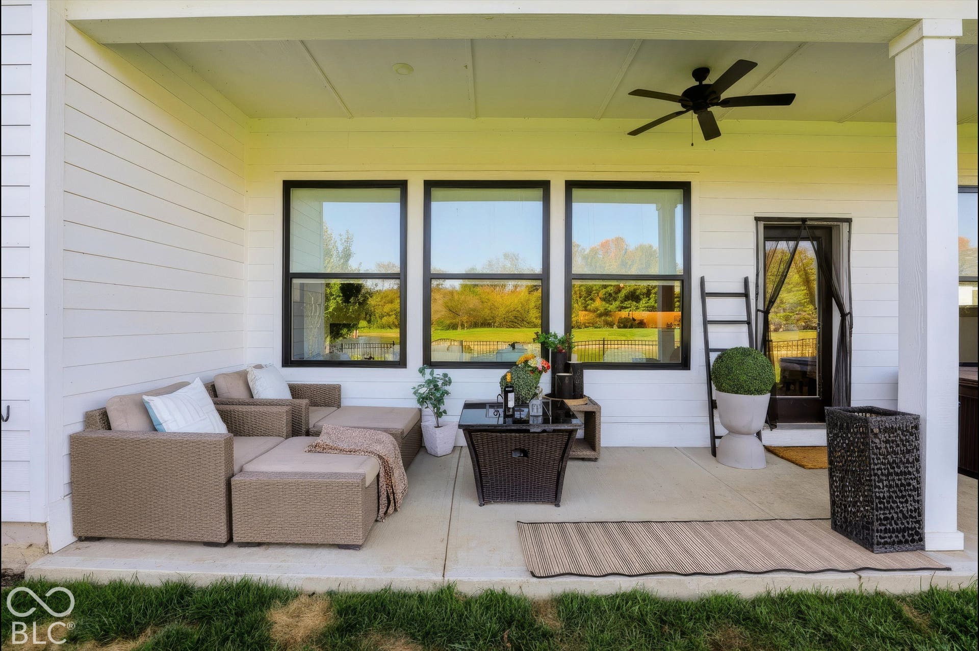 Covered patio featuring concrete flooring, horizontal lap siding, ceiling-mounted fan, and large windows with black trim
