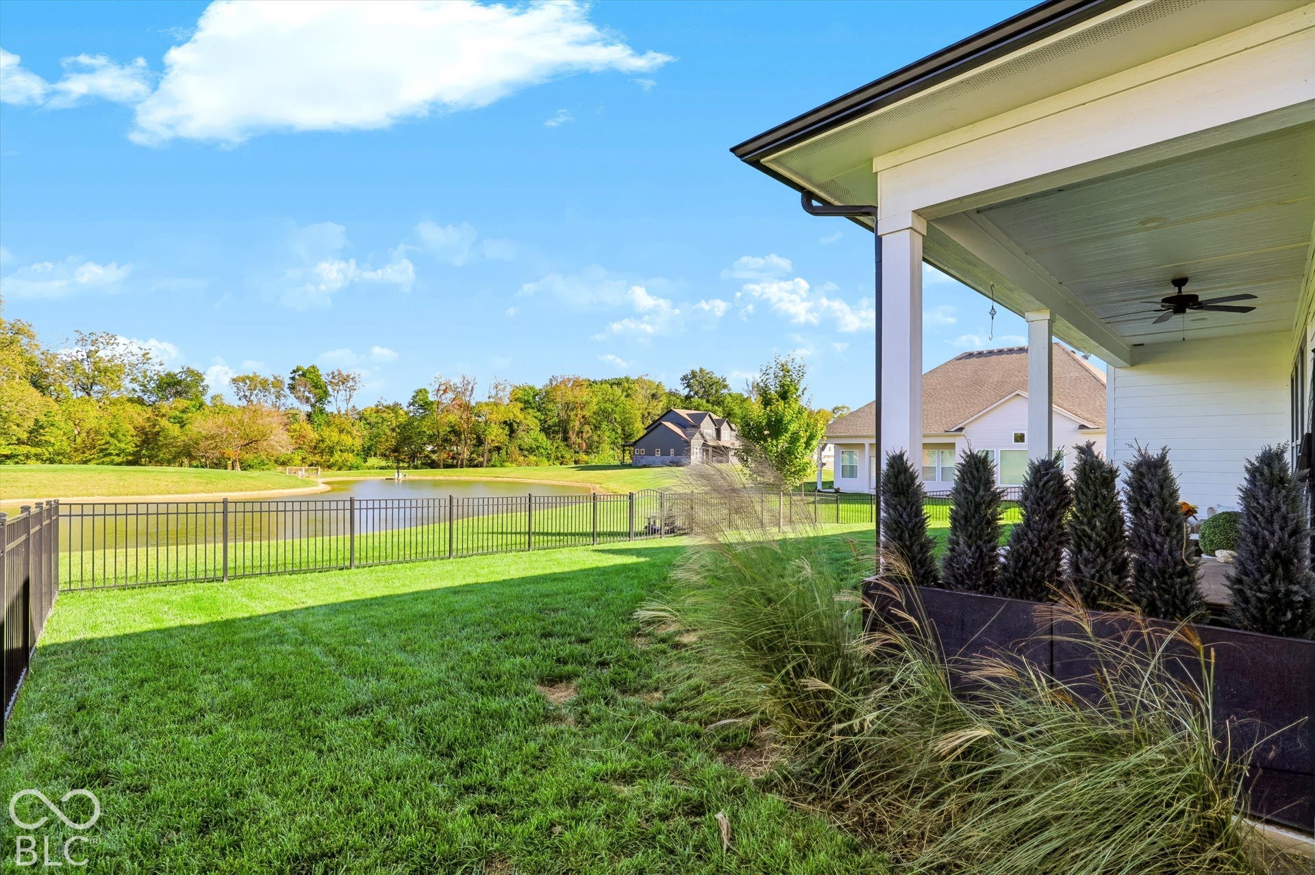 Covered patio featuring a ceiling fan, metal perimeter fencing, manicured lawn, and water frontage