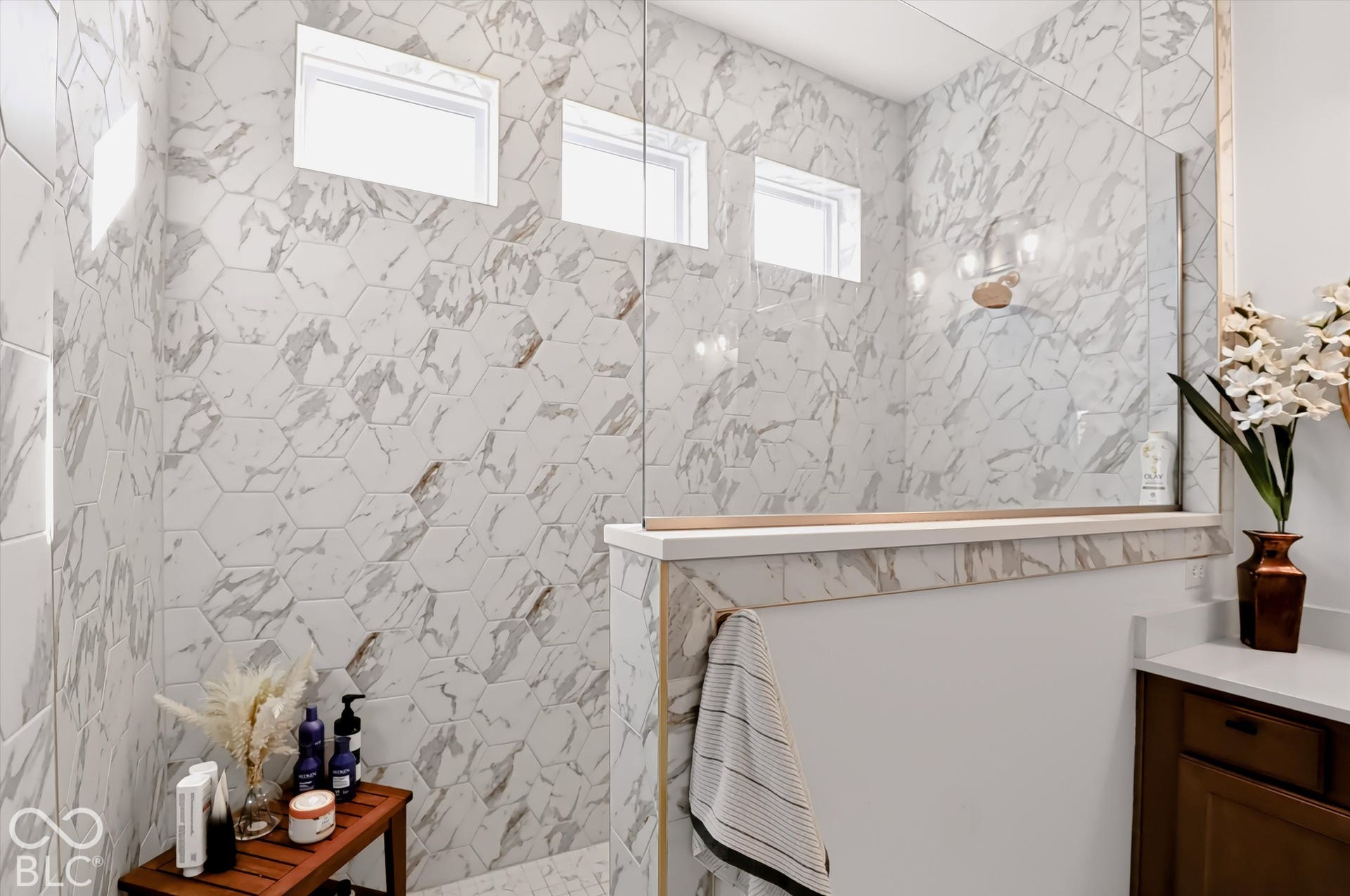 Walk-in shower featuring large-format hexagonal wall tile, a glass partition, three inset windows, and a capped half-wall