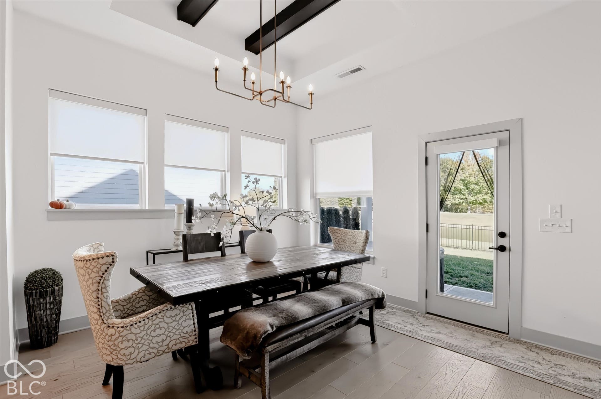 Dining area featuring a tray ceiling with exposed structural beams, wood-finish flooring, multi-pane casement windows, and a multi-arm metal chandelier