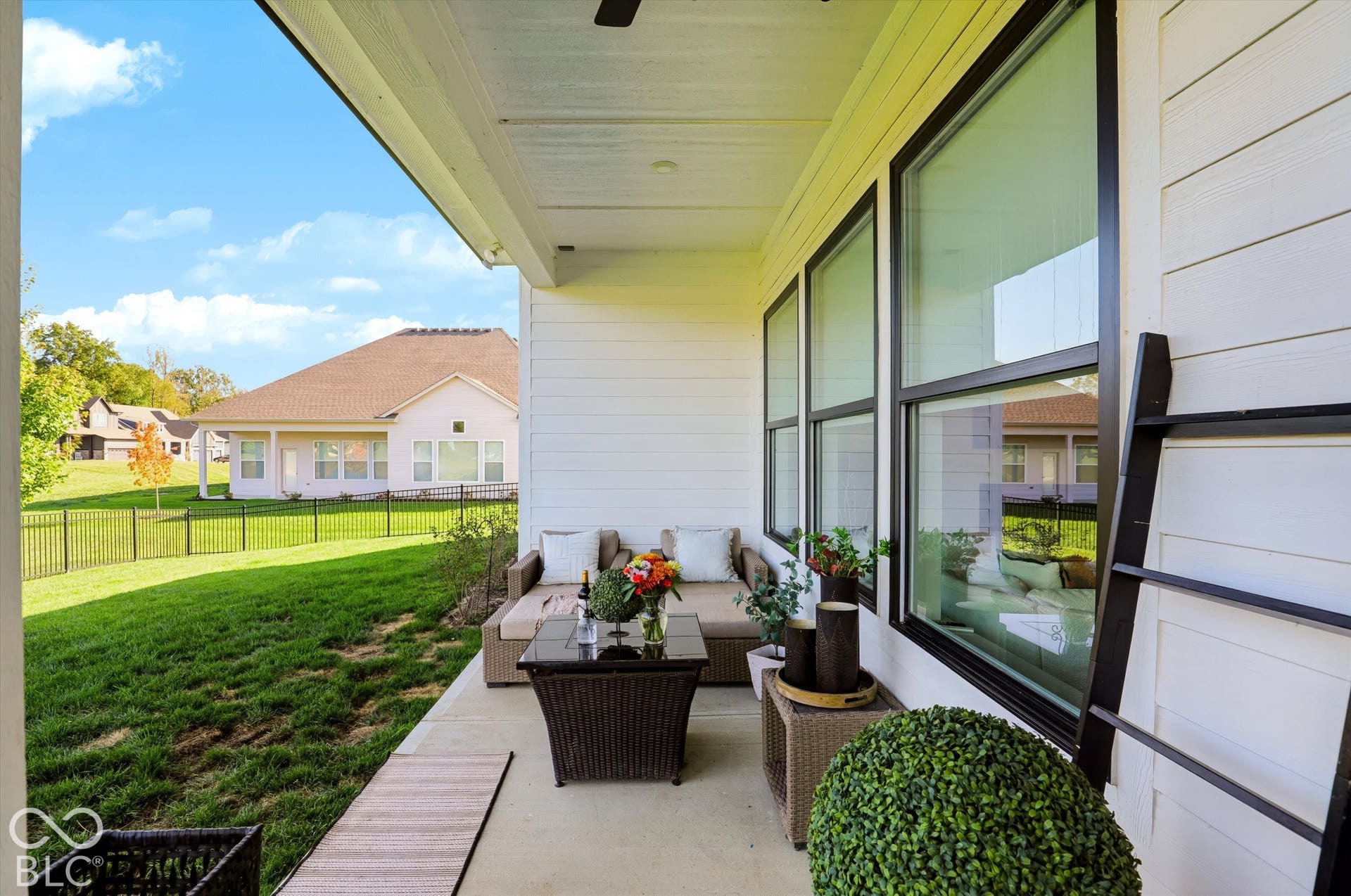 Covered concrete patio featuring horizontal lap siding, expansive windows with dark frames, and a metal perimeter fence