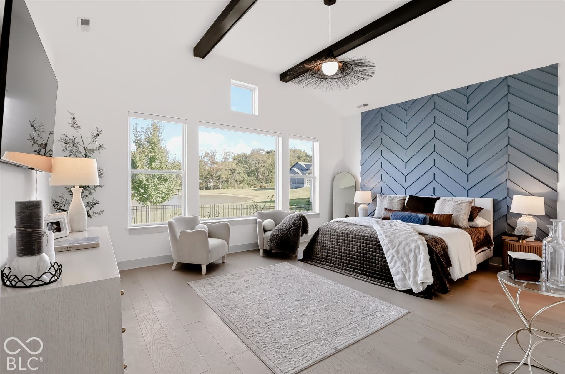 Vaulted ceilings with exposed beams, herringbone-patterned accent wall, wide-plank wood-finish flooring, and large windows