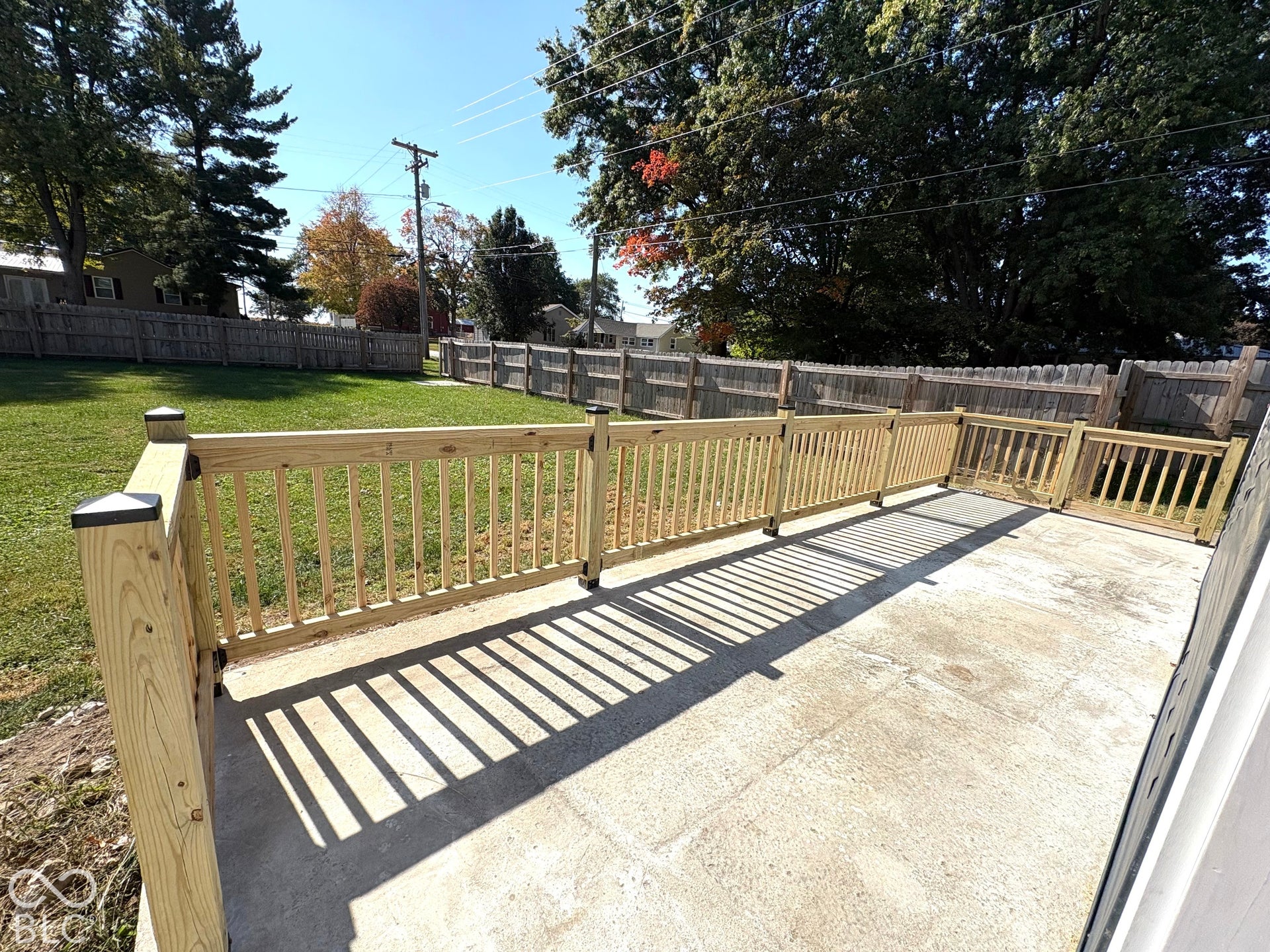 Concrete patio featuring a wood-rail perimeter fence, gated enclosure, and expansive lawn area