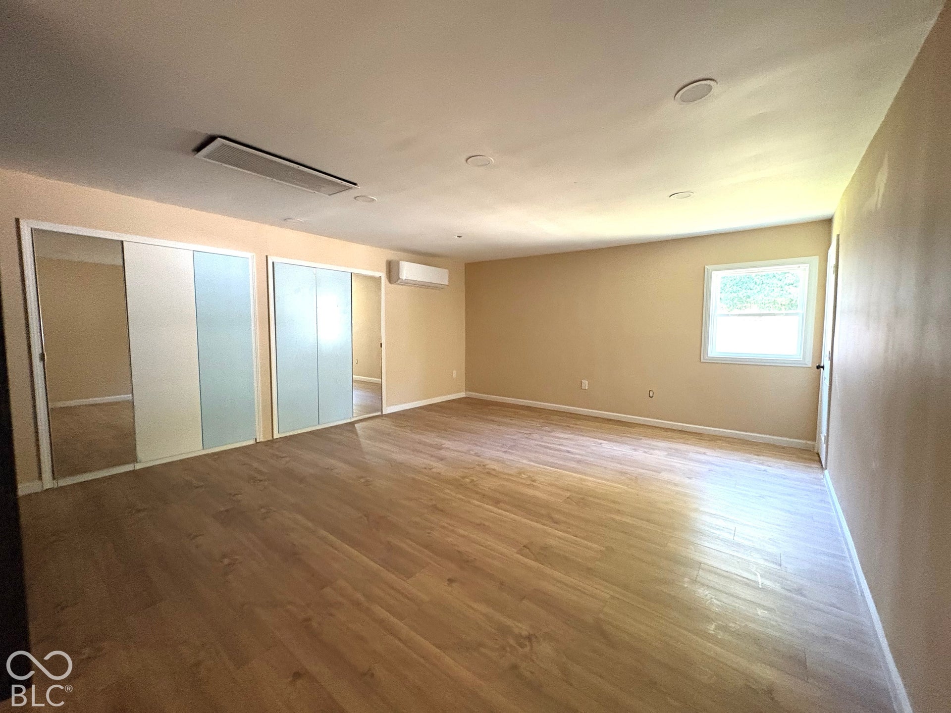 Room featuring wood-finish flooring, recessed lighting, dual sliding-mirror door closets, and a wall-mounted climate control unit