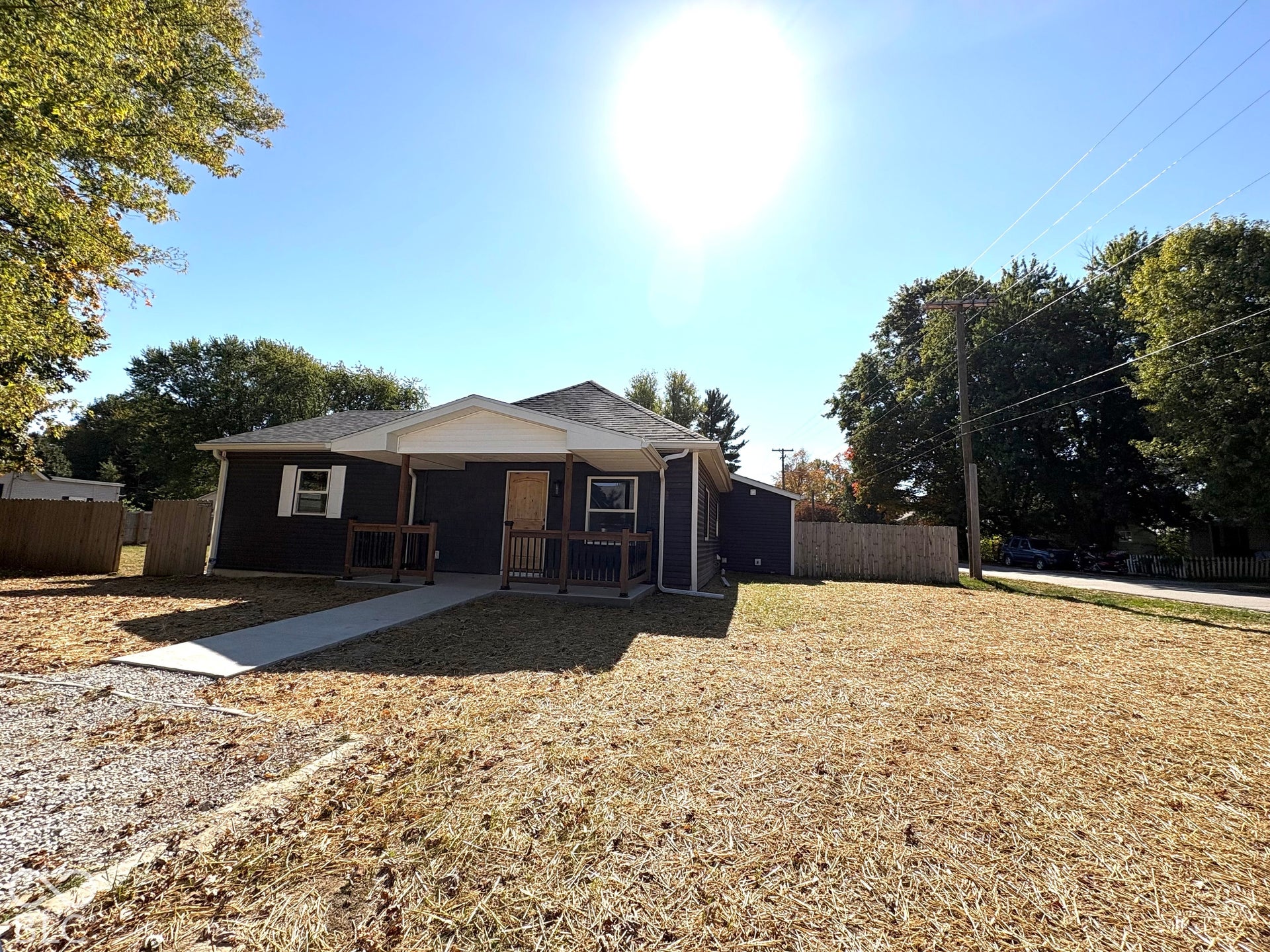 Single-story exterior featuring dark-toned horizontal siding, a covered front porch with wooden railings, a concrete walkway, and wood-finish front door