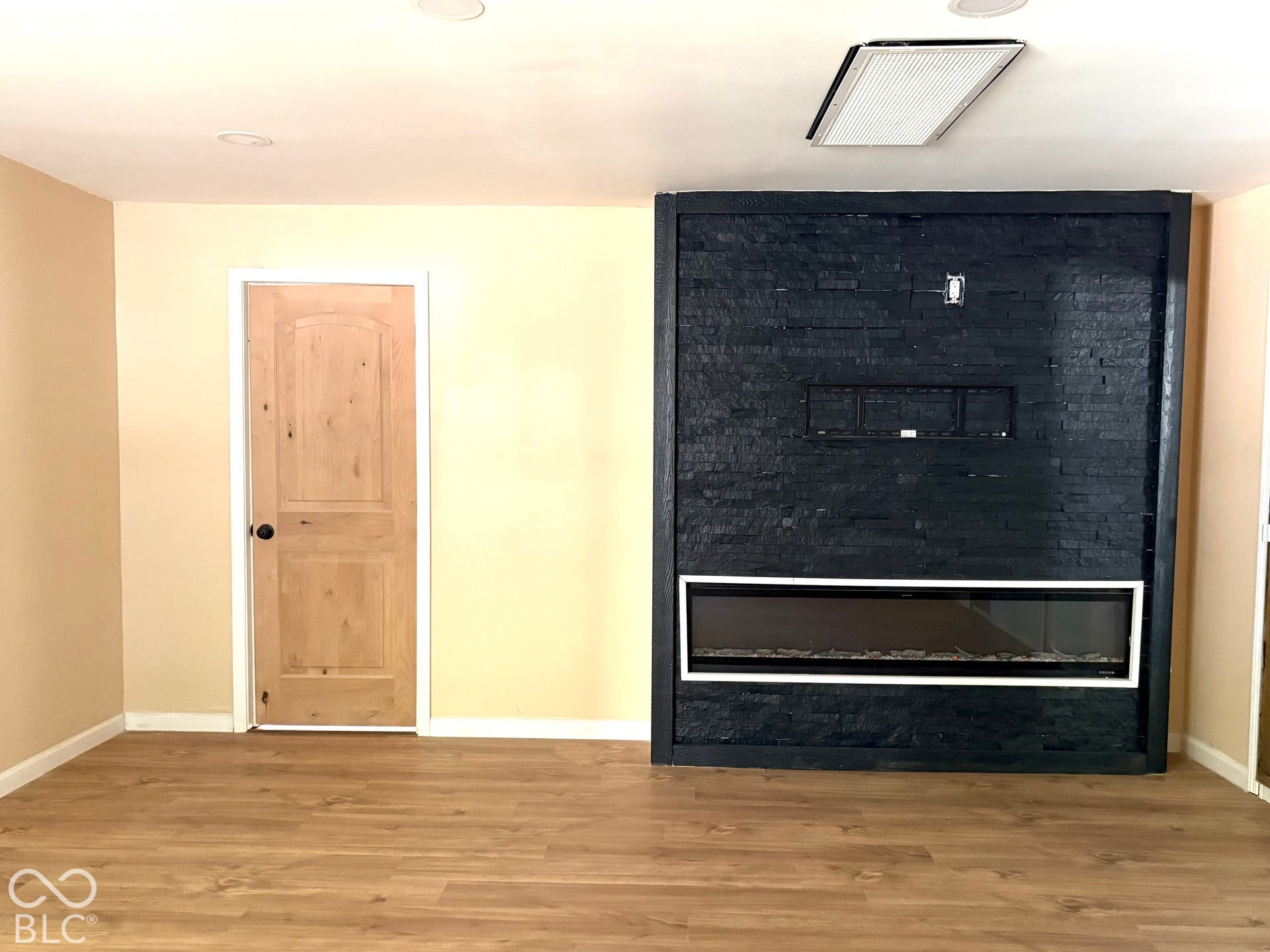 Black stacked stone fireplace surround with a linear insert, wood-finish flooring, and a natural wood-finish interior door