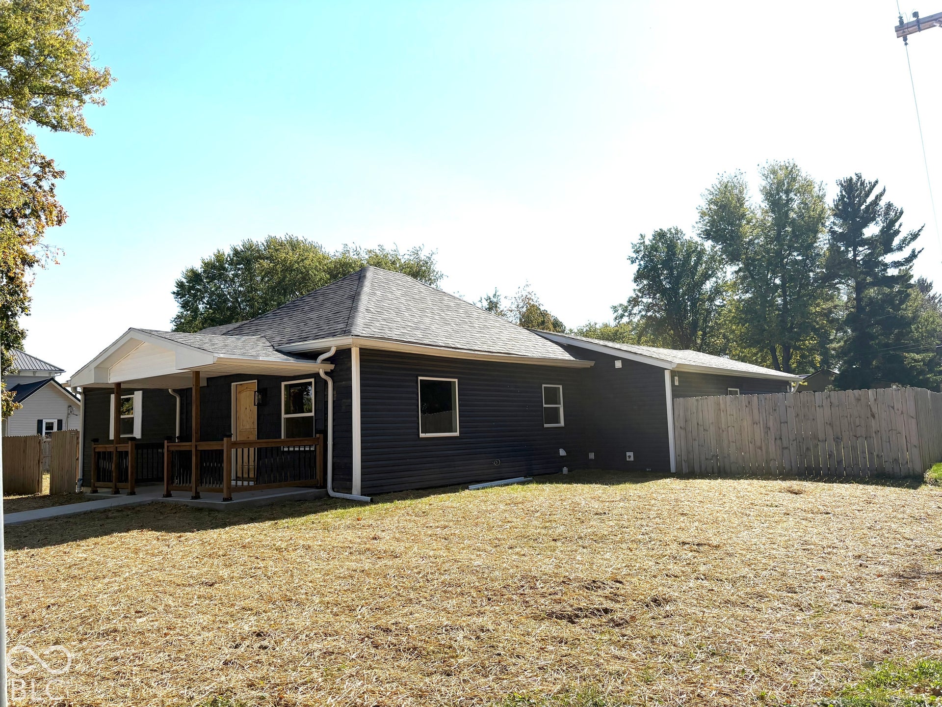Dark-toned exterior siding featuring a covered front porch with wooden railings and a privacy fence