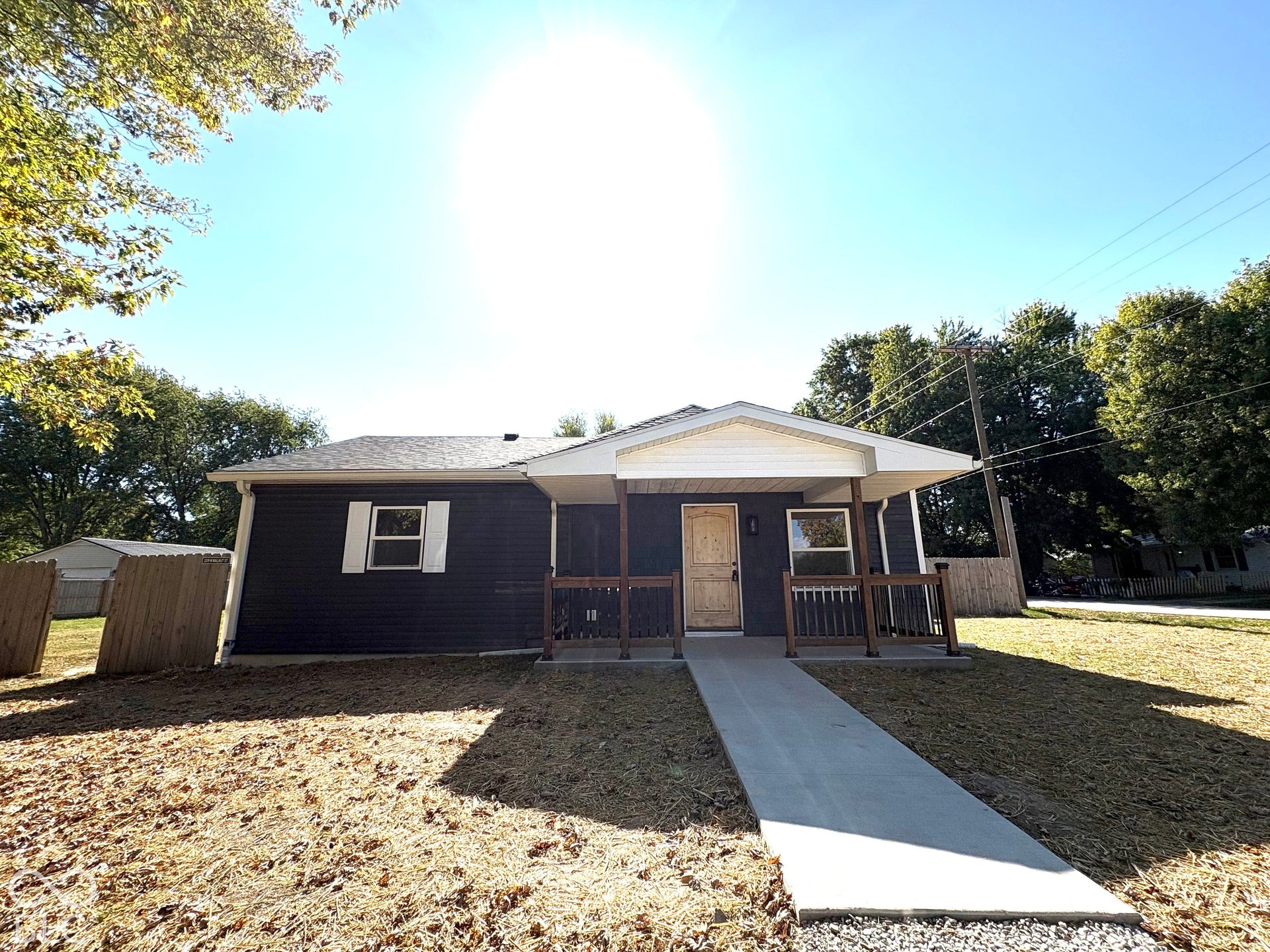 Dark-toned siding exterior featuring a concrete front walkway, covered porch with wood-finish railing, and white shutter accents