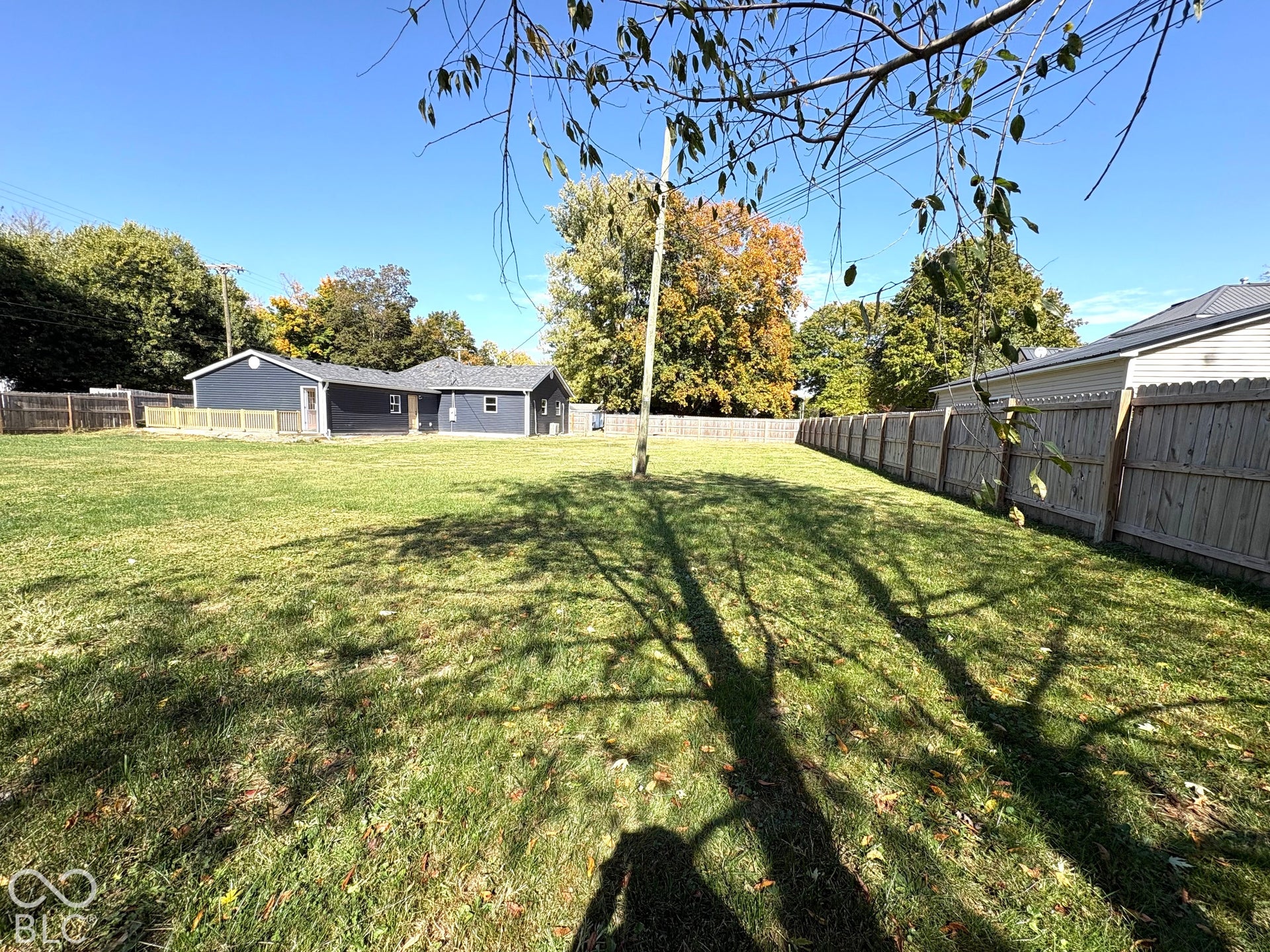 Expansive backyard featuring a large grass lawn, perimeter wood fencing, and mature trees