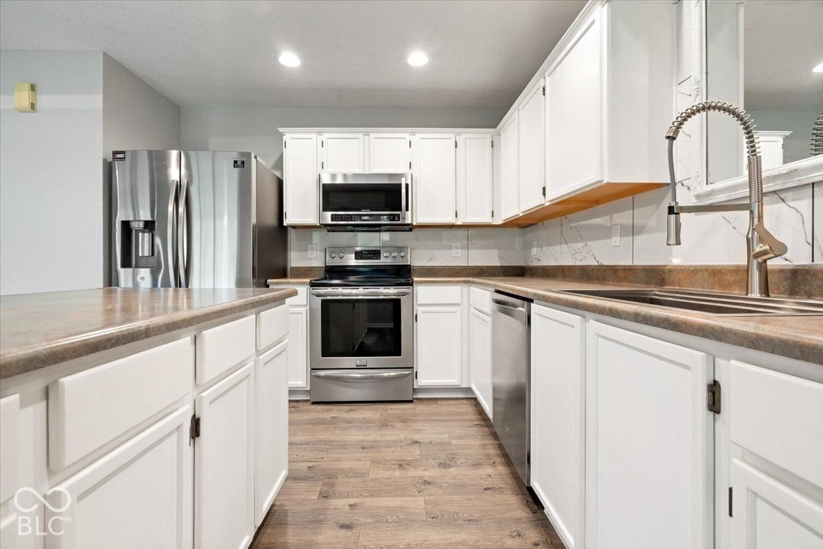 Kitchen featuring white shaker-style cabinetry, stainless steel appliances, stone-patterned backsplash, wood-finish flooring, and a gooseneck pull-down faucet
