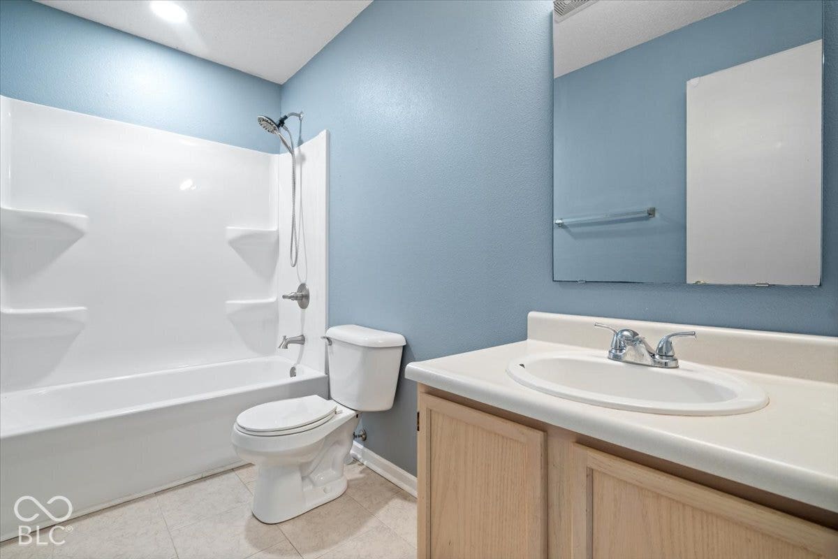 Bathroom featuring a vanity with an integrated countertop sink, metal dual-handle faucet, wall-mounted mirror, and a full-size tub and shower combination with molded shelving