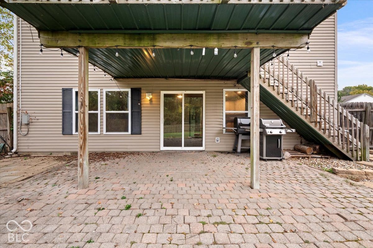 Rear exterior featuring a paver patio, covered porch with metal roofing, sliding glass door, vinyl siding, and exterior wooden staircase